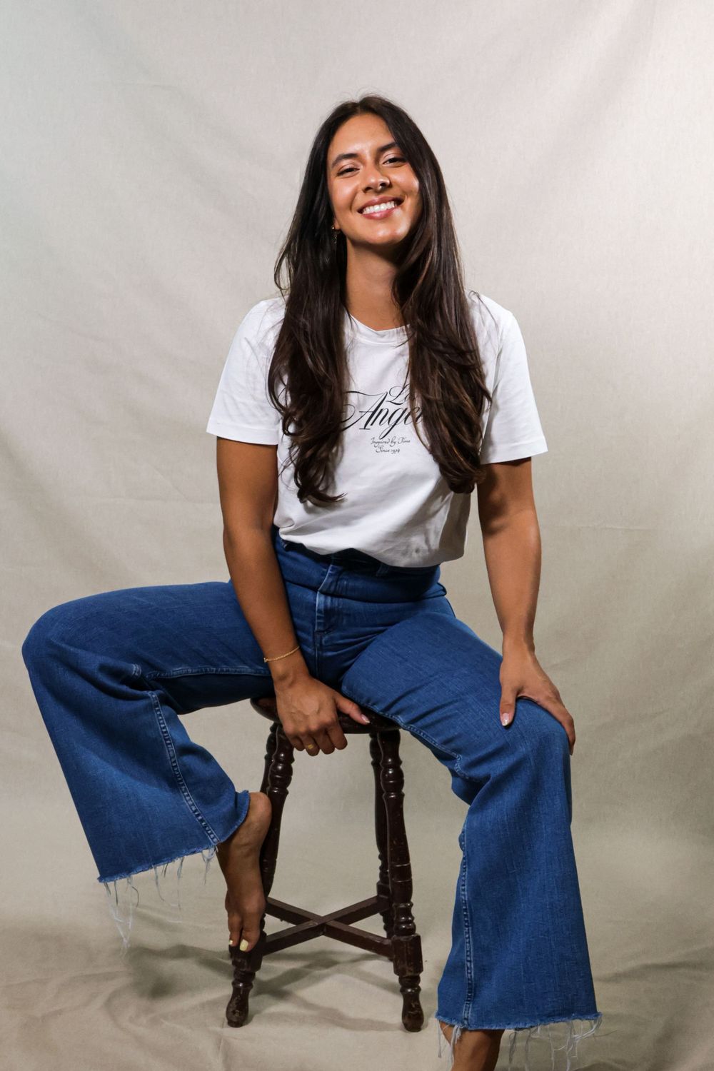 Person wearing white t-shirt and jeans sitting casually on wooden chair.