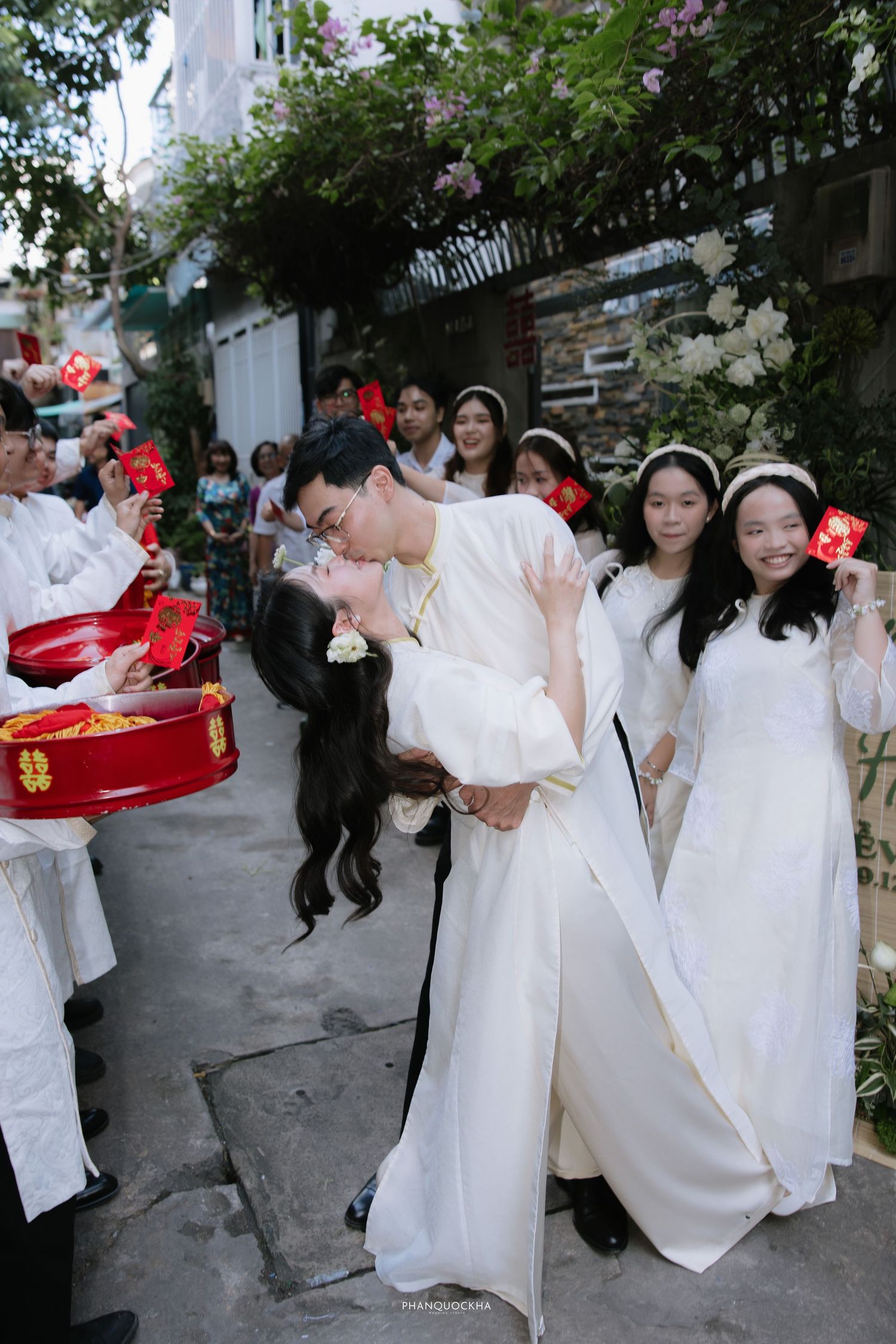 Groom lifts bride for a kiss during a joyful Vietnamese traditional wedding procession outdoors.