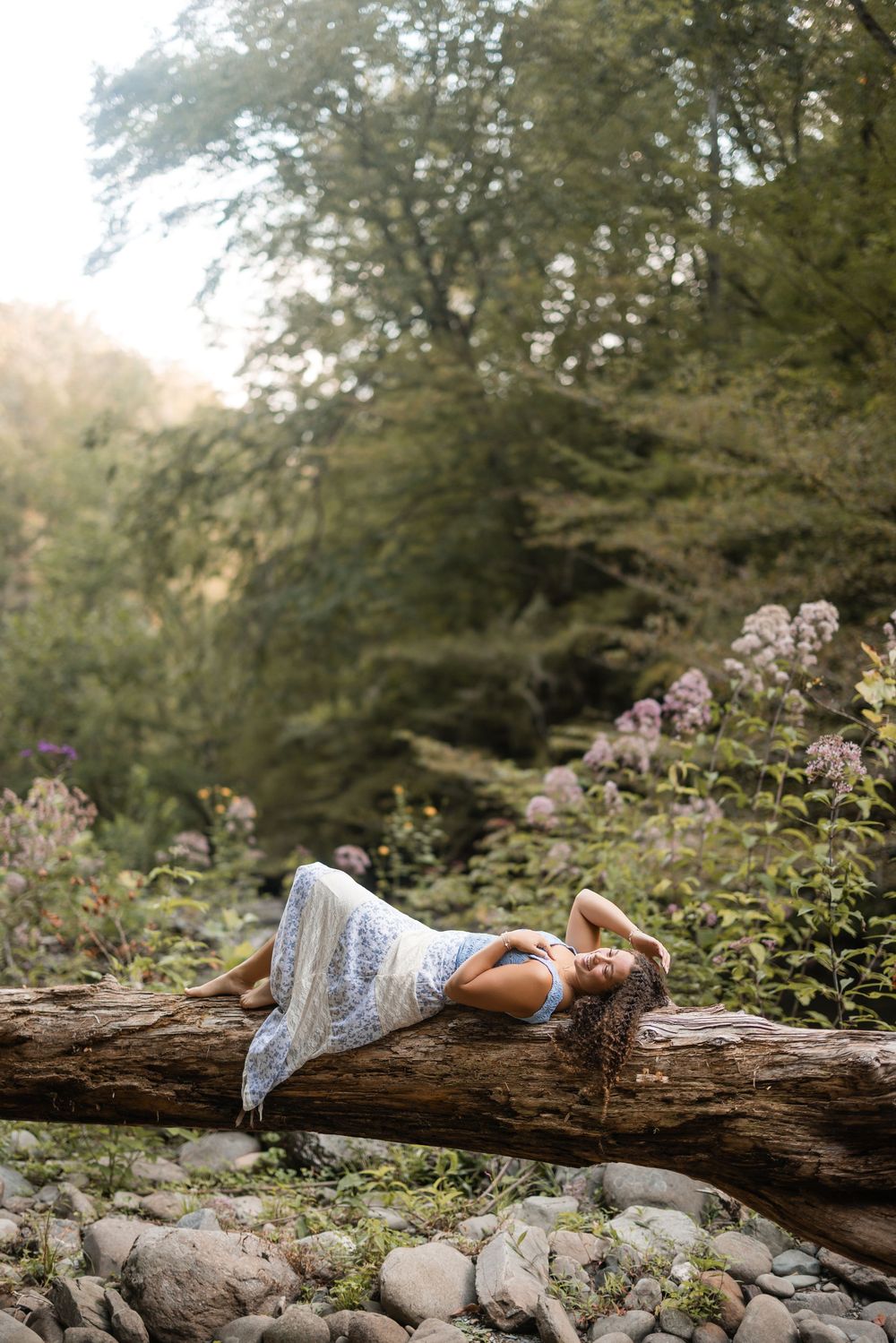 A dreamy outdoor portrait on a fallen log surrounded by wildflowers and greenery in soft natural lighting.