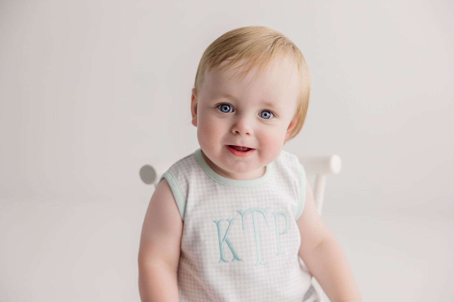 Sweet baby in white romper sitting on light background during minimalist cake smash photo session.