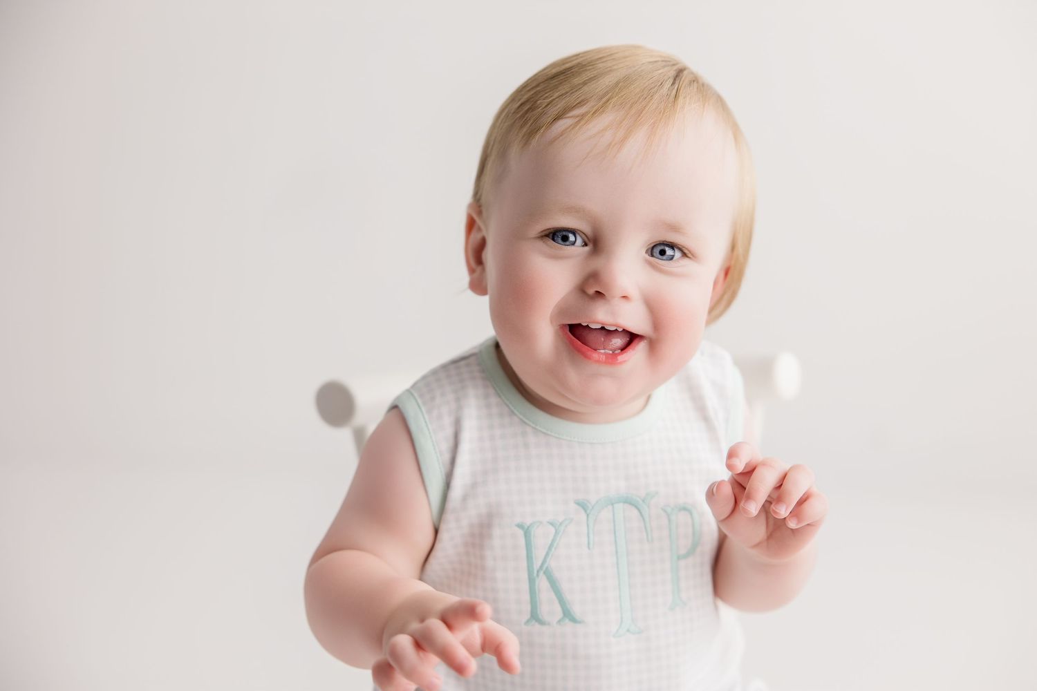 Happy baby in white outfit reaching up during studio portrait session.