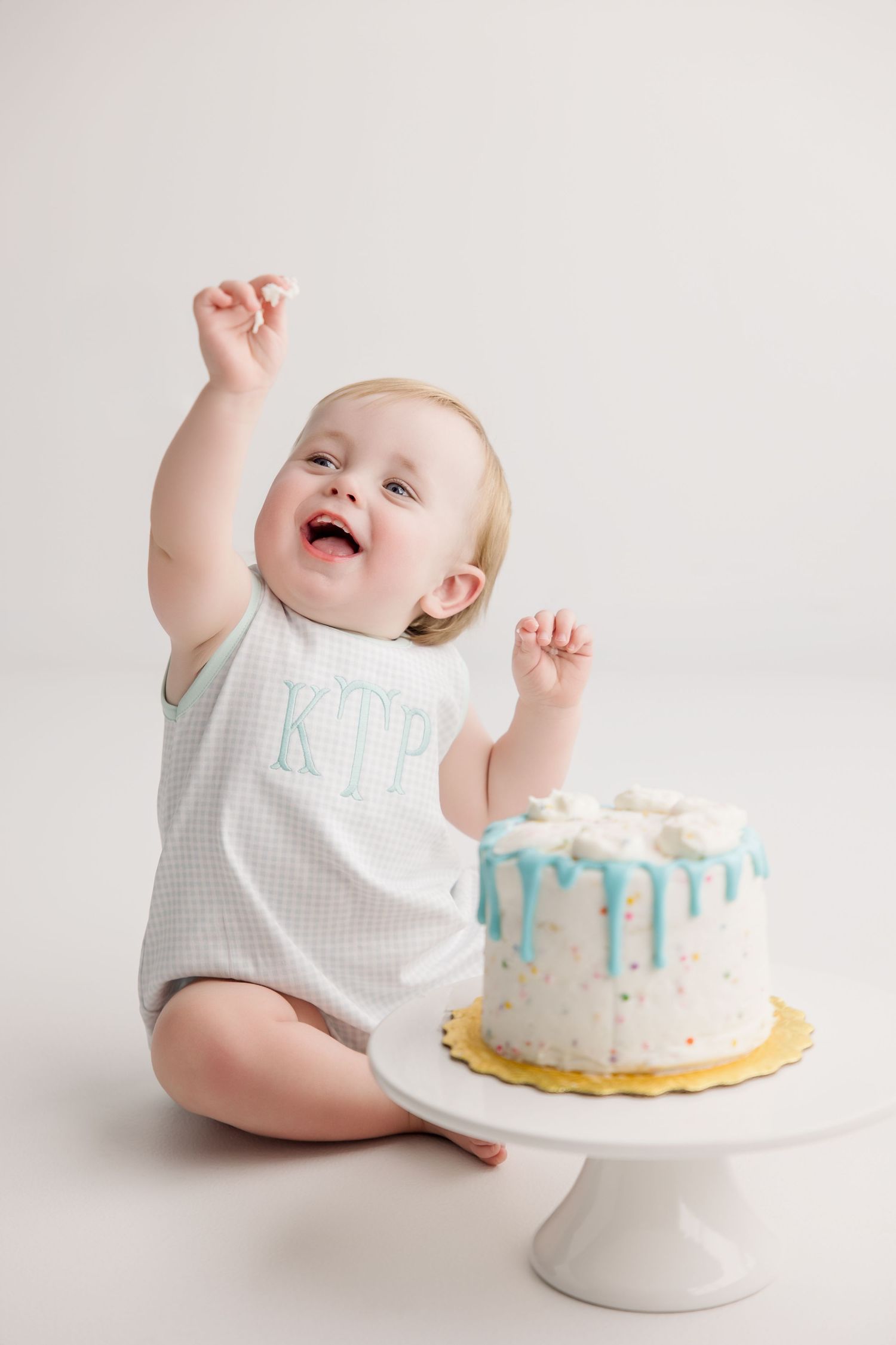 Joyful movements and expressions near a white birthday cake with blue accents on a cake pedestal.
