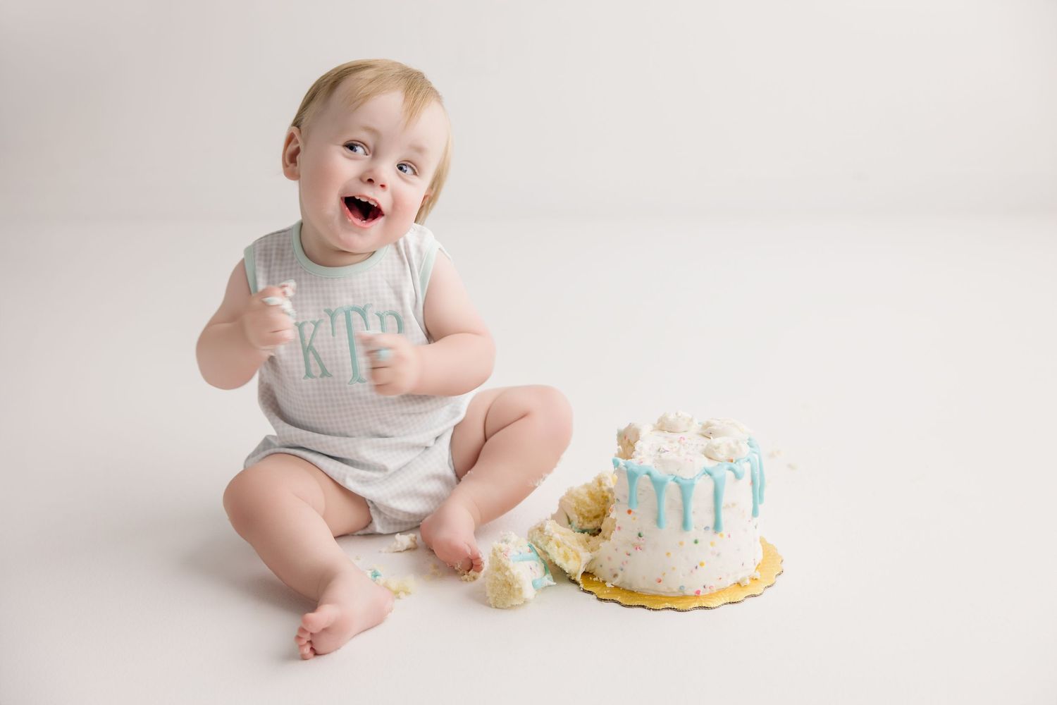 Sweet first birthday celebration scene with white cake and turquoise decorations on white backdrop.