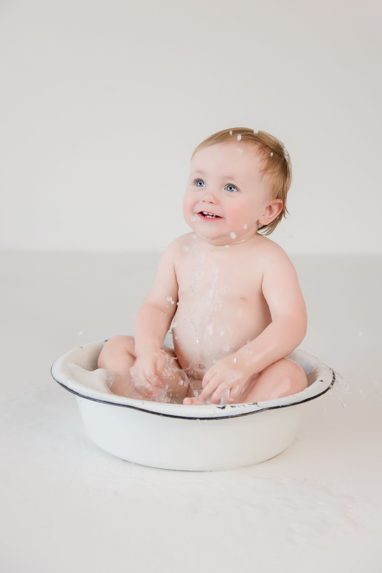 Small child sitting in vintage enamel basin during milk bath photo session against white background.