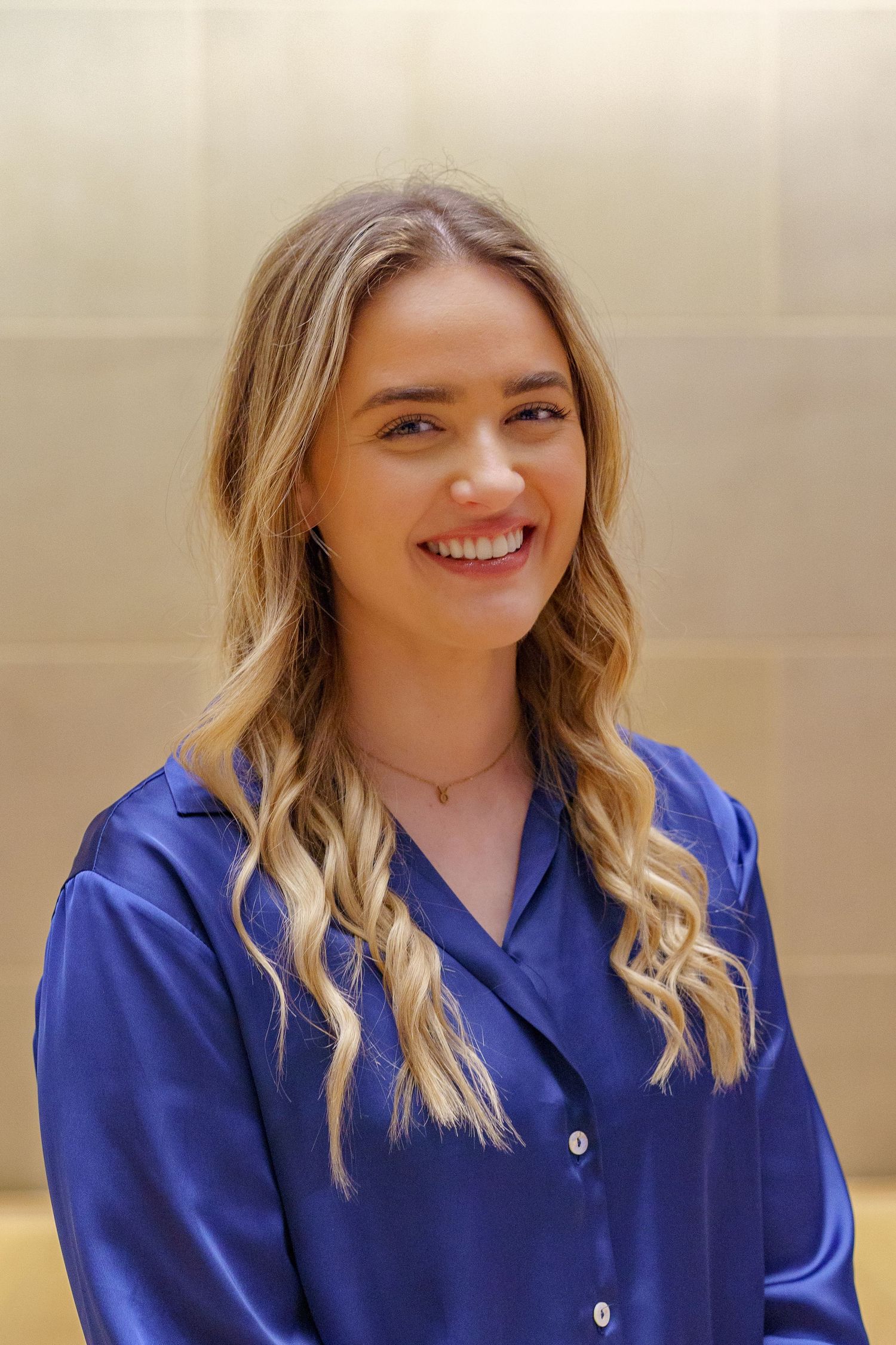Young lady smiling for her headshot, indoors with a sandstone background