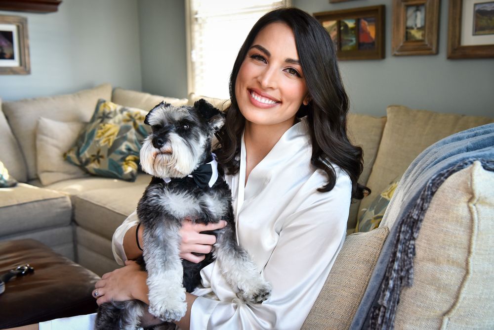 A person in a white bathrobe enjoys a heartwarming moment on the couch with their small black and gray schnauzer dog.