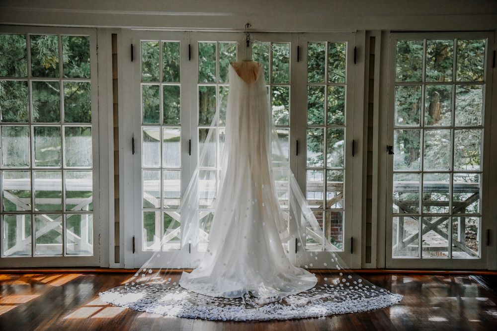 Three identical white wedding dresses on display hang in a row of beautiful sunlit windows.