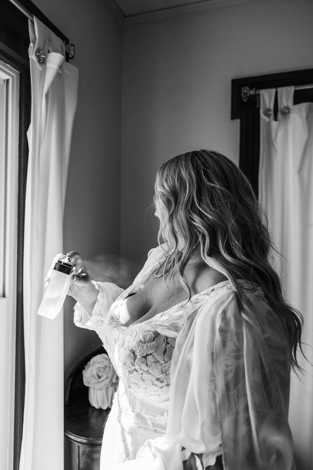 candid black & white image of bride spraying perfume in bridal suite at Sister Hill venue in Manchester Iowa by midwest wedding photographer
