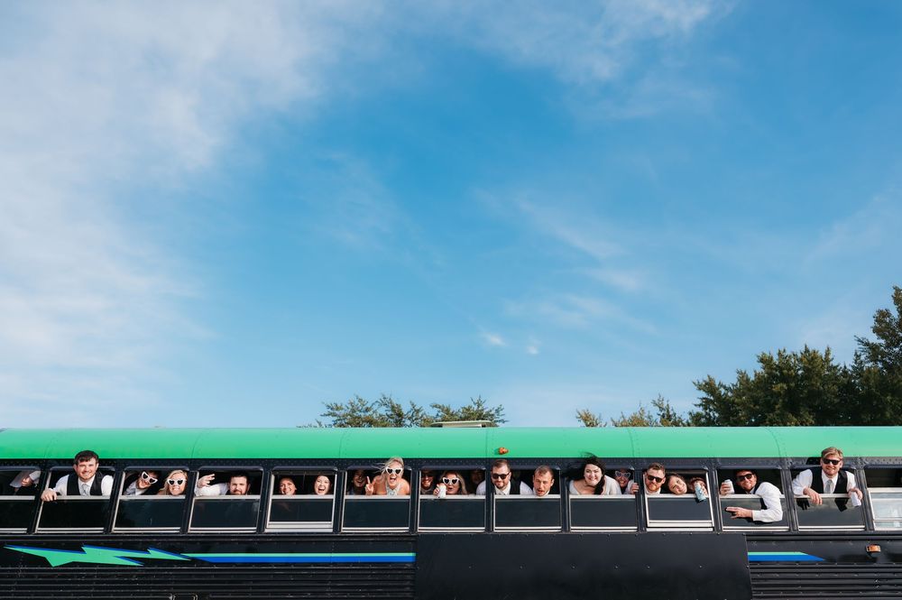 party bus with bridal party poking heads out the windows for picture. bright blue skies taken by iowa midwest wedding photographer