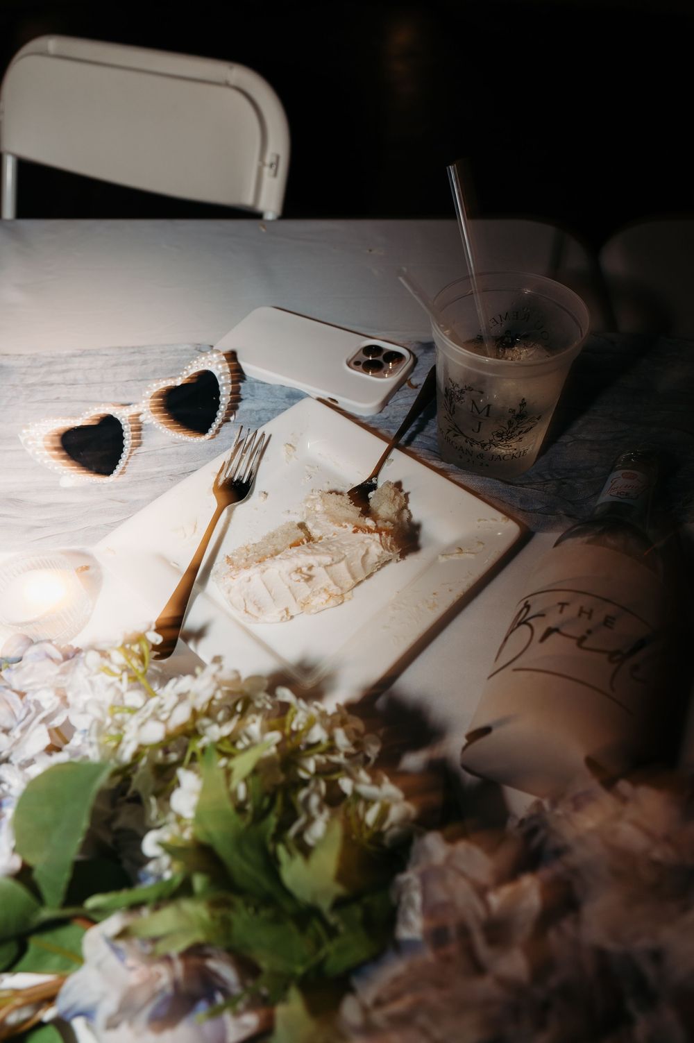 late night blurred detail image of cake plate, drink, sunglasses & bride koozie with flowers at Denali's on the River Independence Iowa