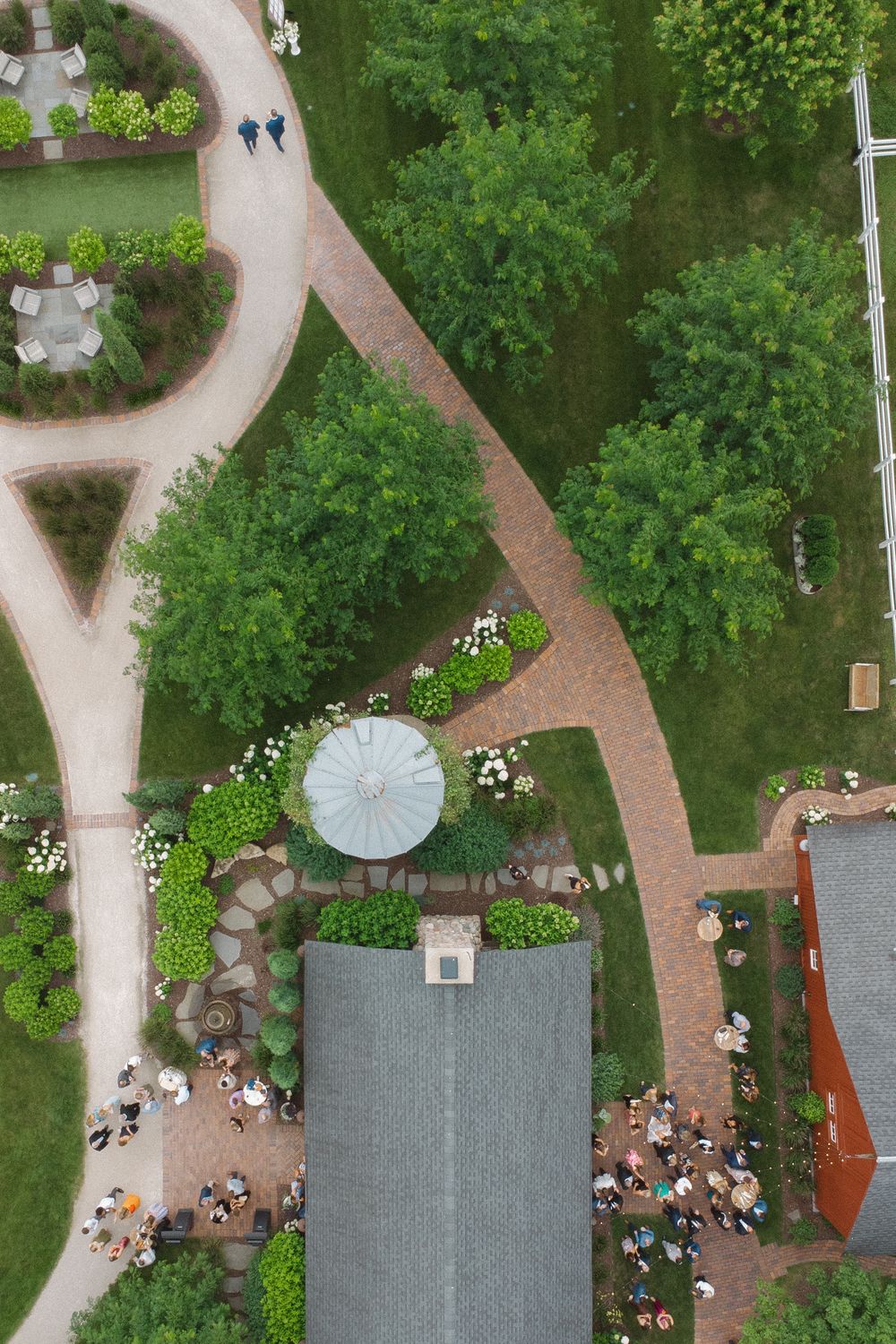 Aerial view of a wedding reception venue with brick pathways and lush greenery surrounding a red barn structure.