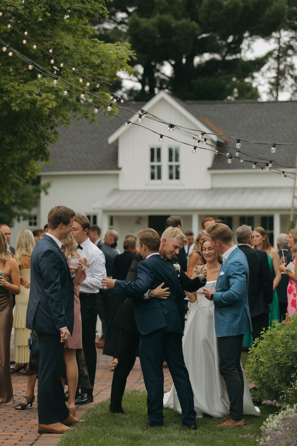 Wedding guests gathered in a receiving line on a brick patio with string lights overhead.