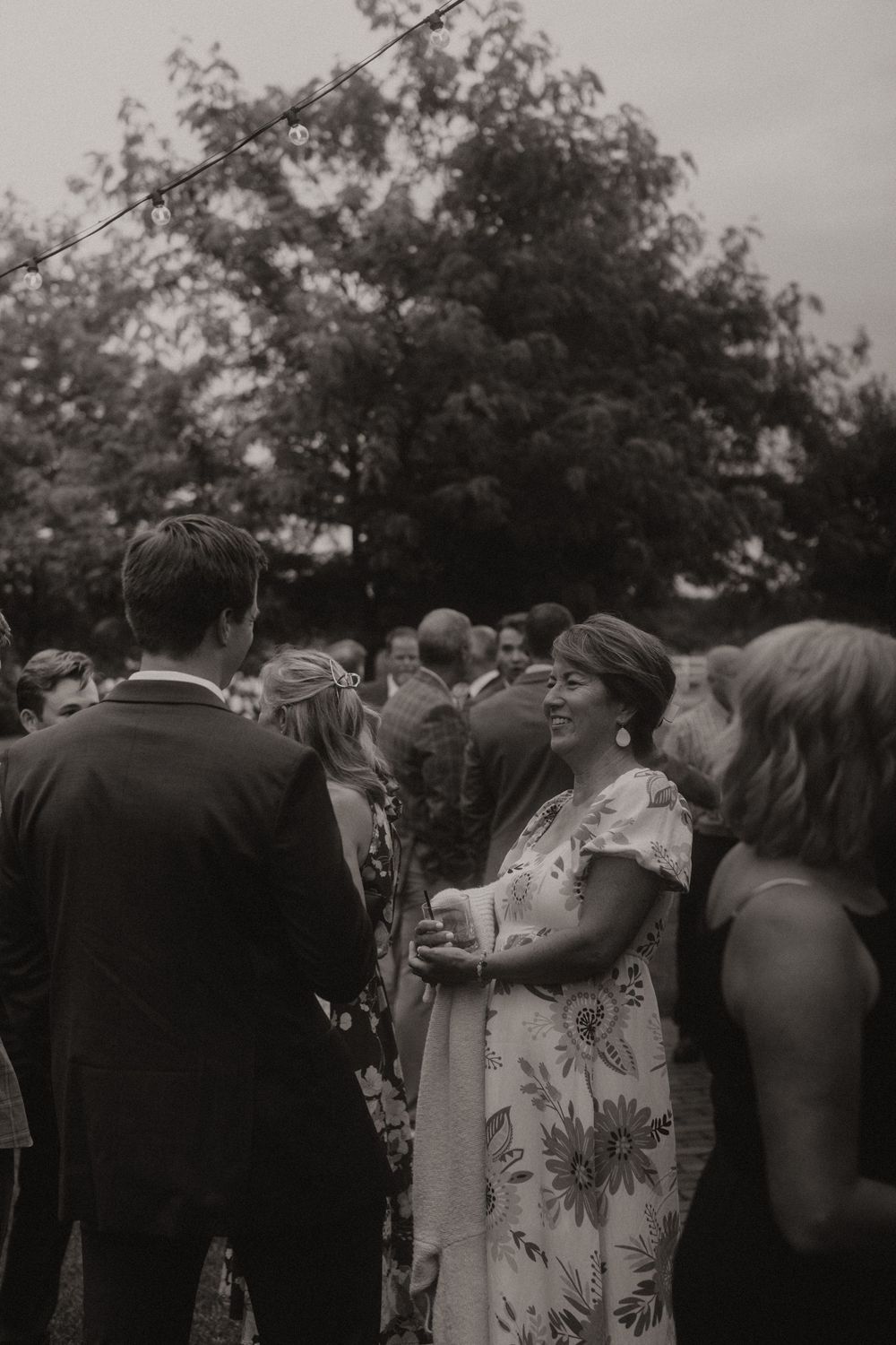 Black and white photo of wedding guests socializing during an outdoor reception.