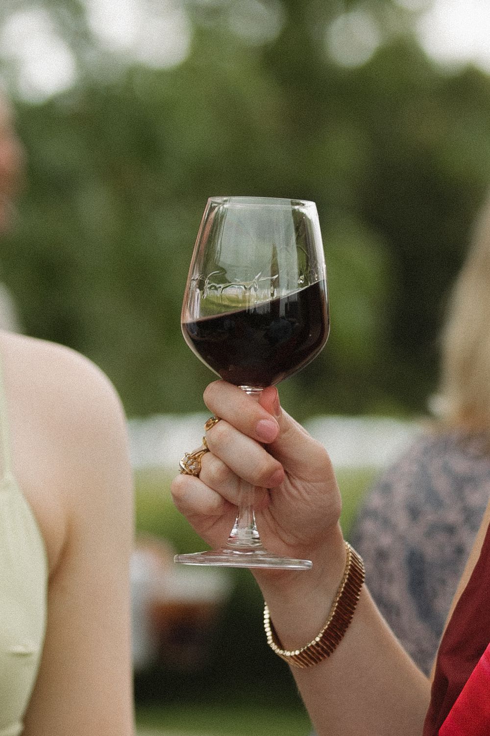 Hand holding a glass of red wine during an outdoor wedding reception.