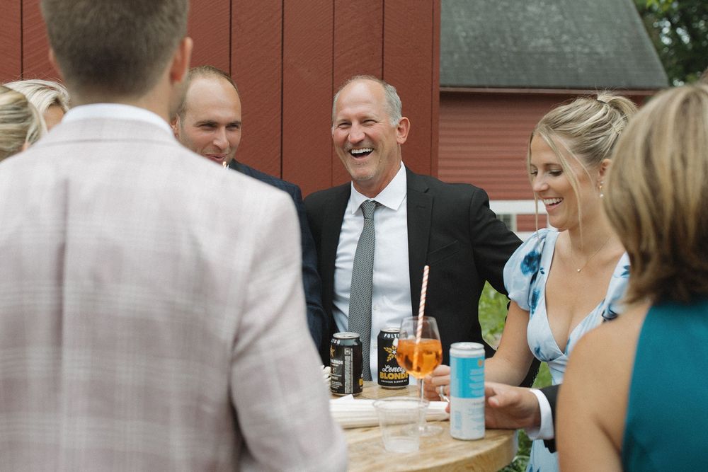 Wedding guests enjoying conversation during outdoor reception by red barn.