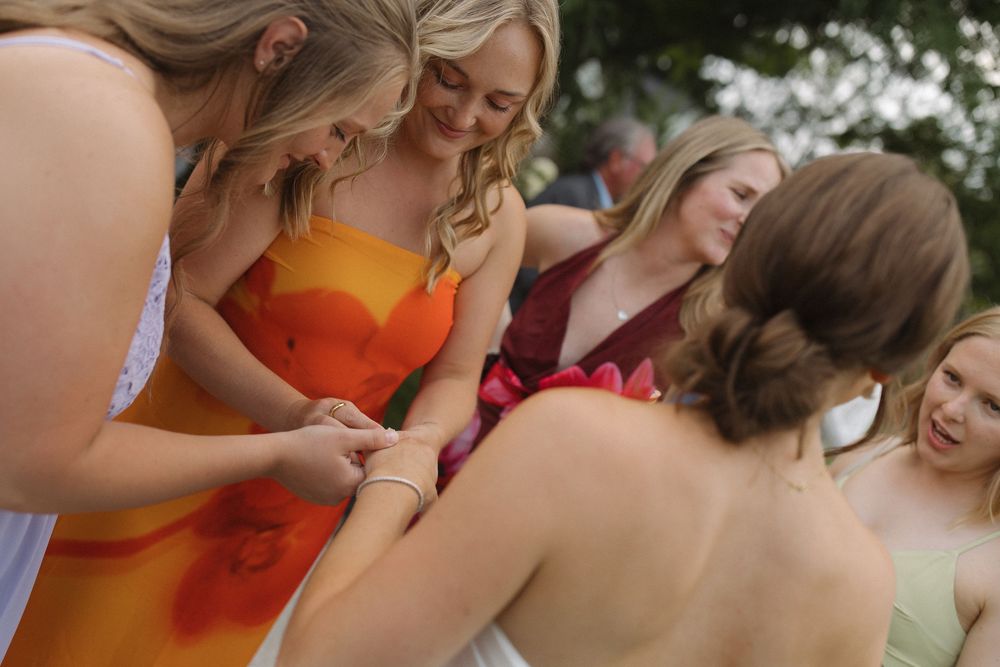 Wedding guests in bright orange and pink dresses mingle during an outdoor reception.