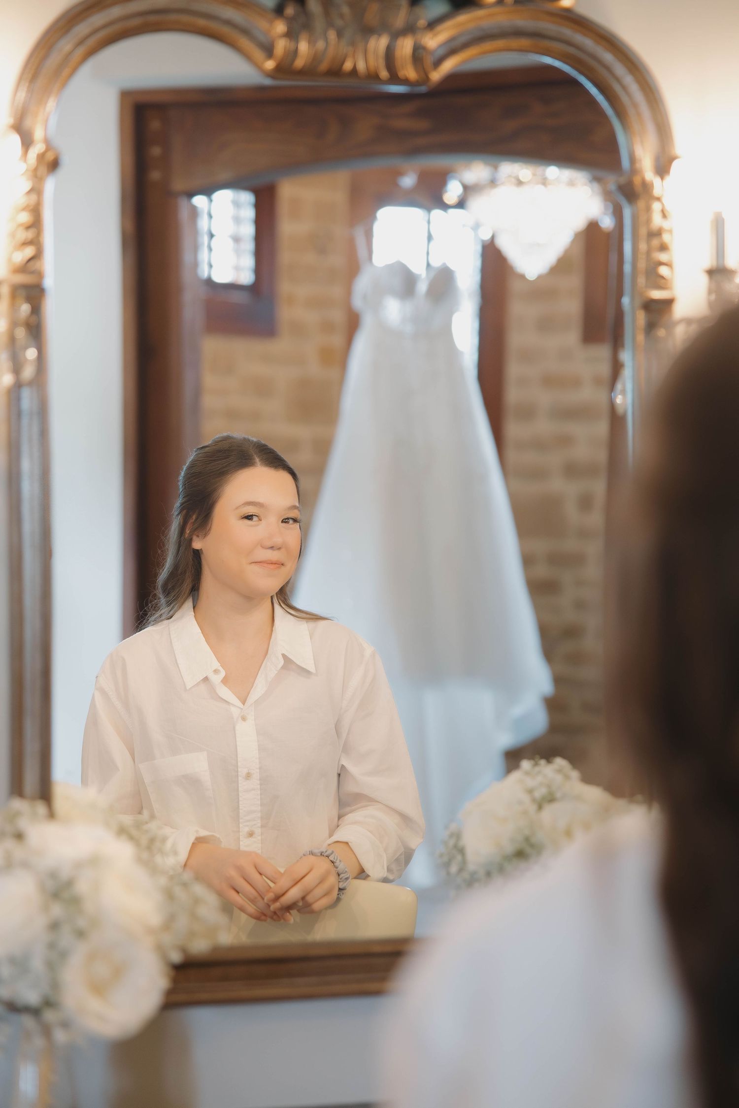 A reflection in an ornate mirror shows a bridal suite with a white wedding dress hanging in the background.