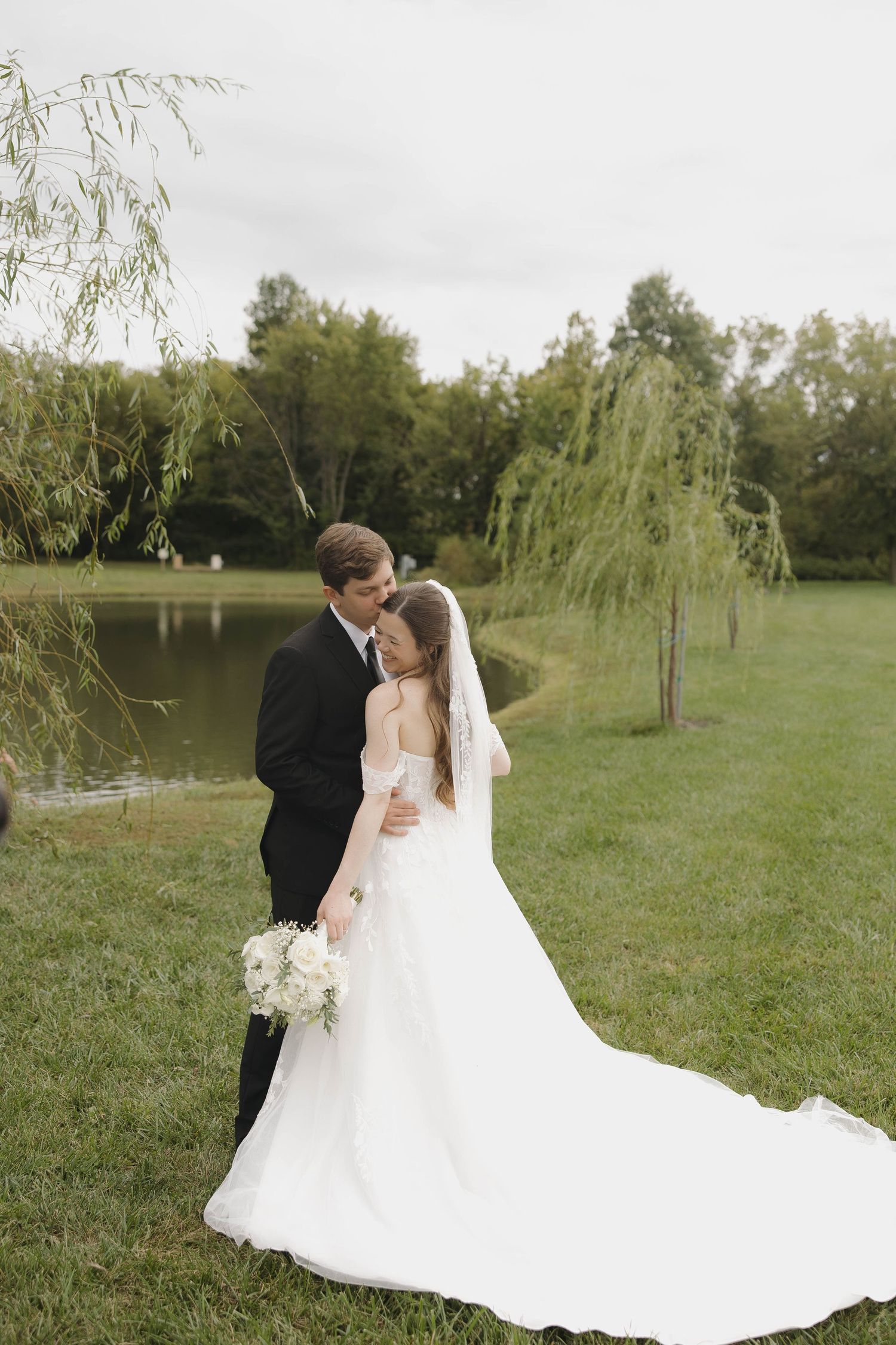 Outdoor wedding couple portrait under weeping willow trees beside a tranquil pond.