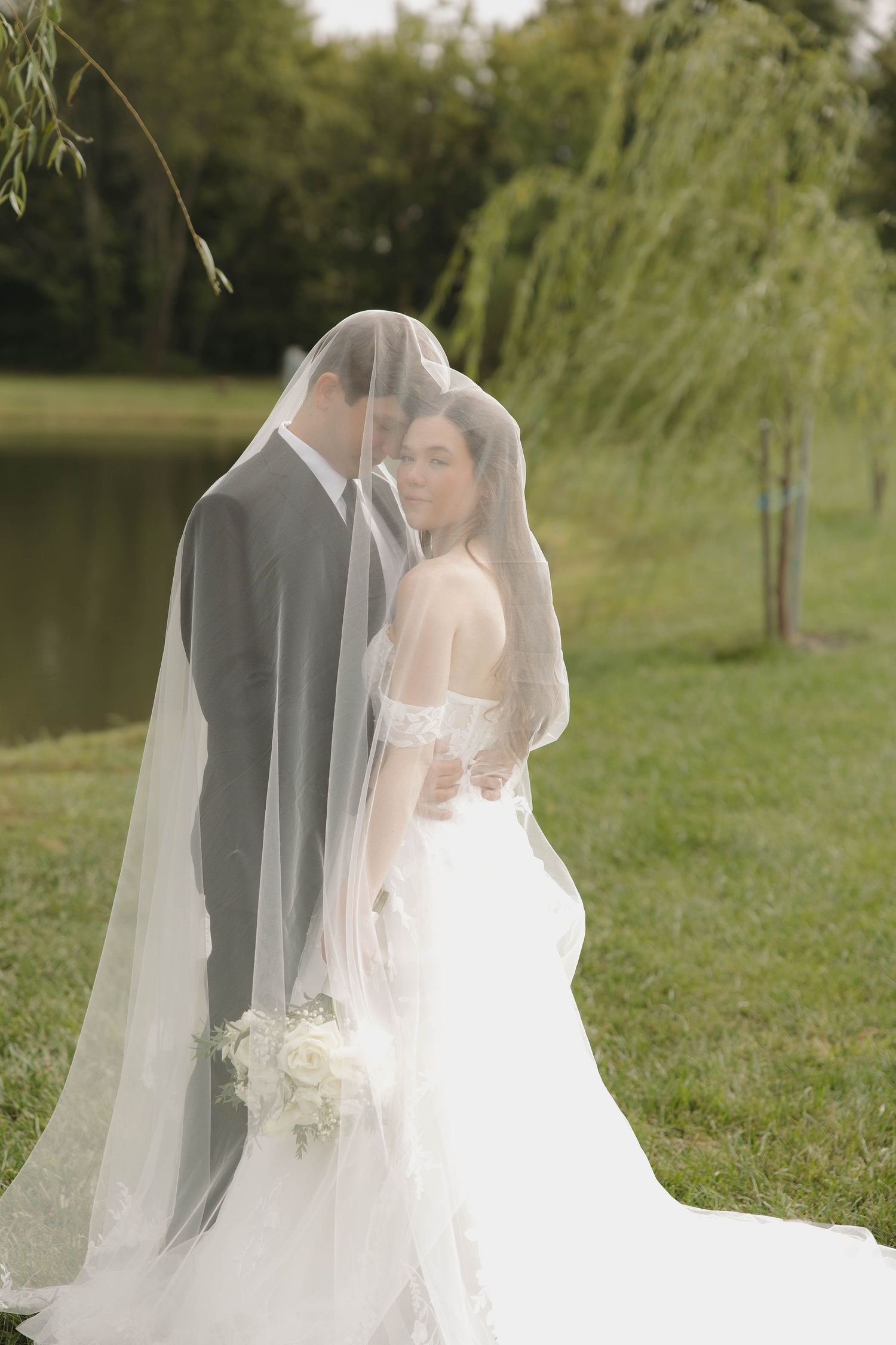 Romantic wedding portrait showing a flowing cathedral veil dancing in the breeze by a tranquil pond.