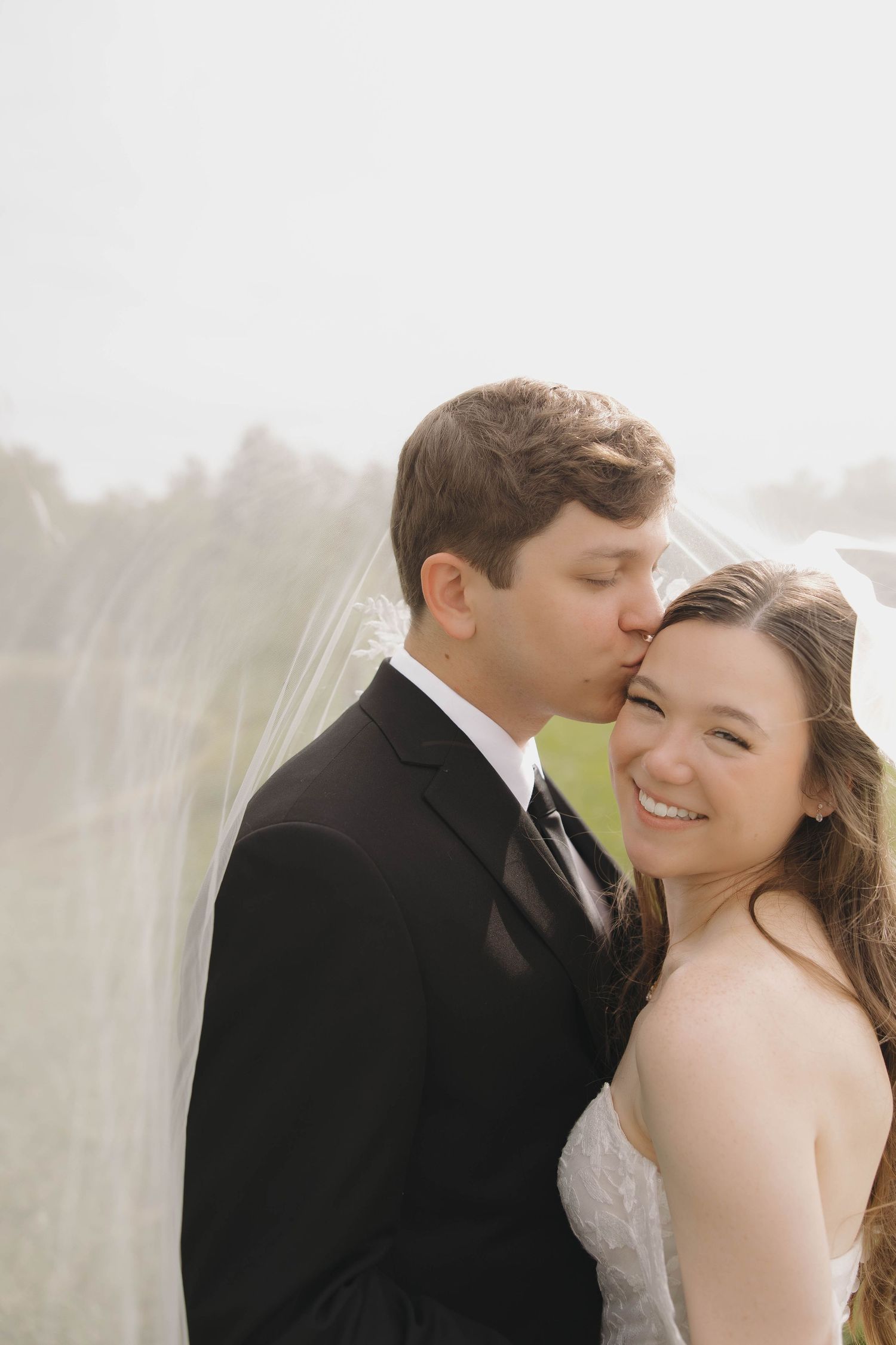 A romantic wedding photo series of a couple embracing outdoors in formal attire with an ethereal misty background.