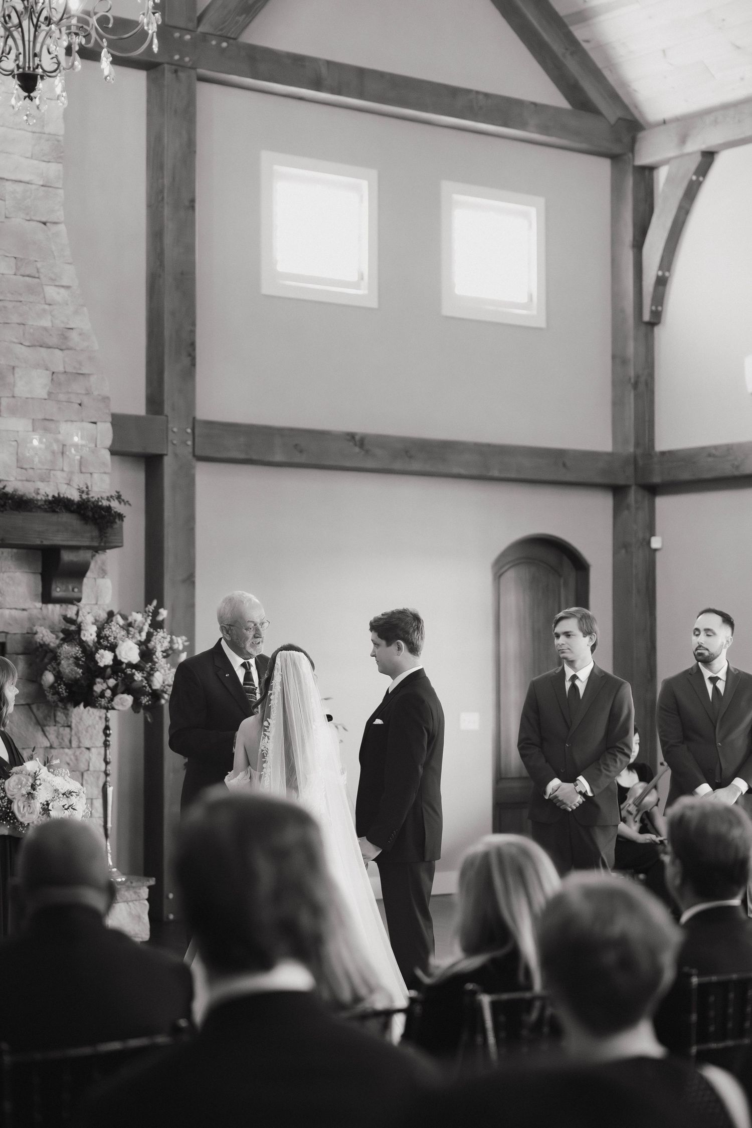 Elegant black and white wedding ceremony in a rustic venue with exposed wooden beams and stone walls.