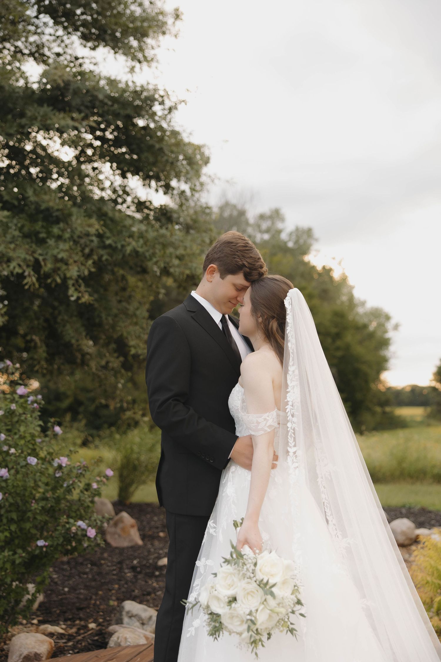 A wedding couple shares an intimate moment together in a garden setting with a beautiful lace veil flowing behind them.