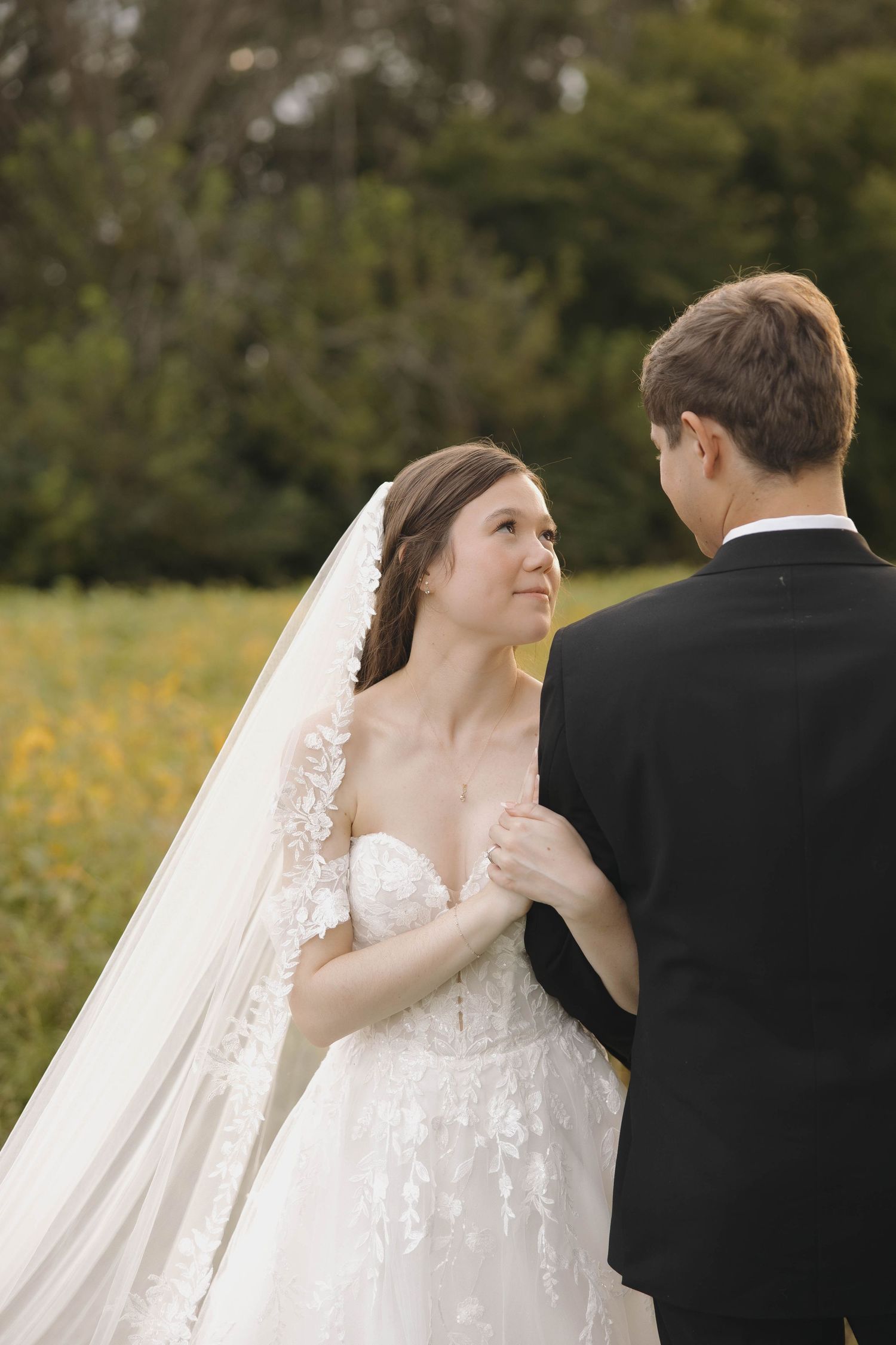 Intimate outdoor wedding moment captured in a field with soft natural lighting and flowing veil.