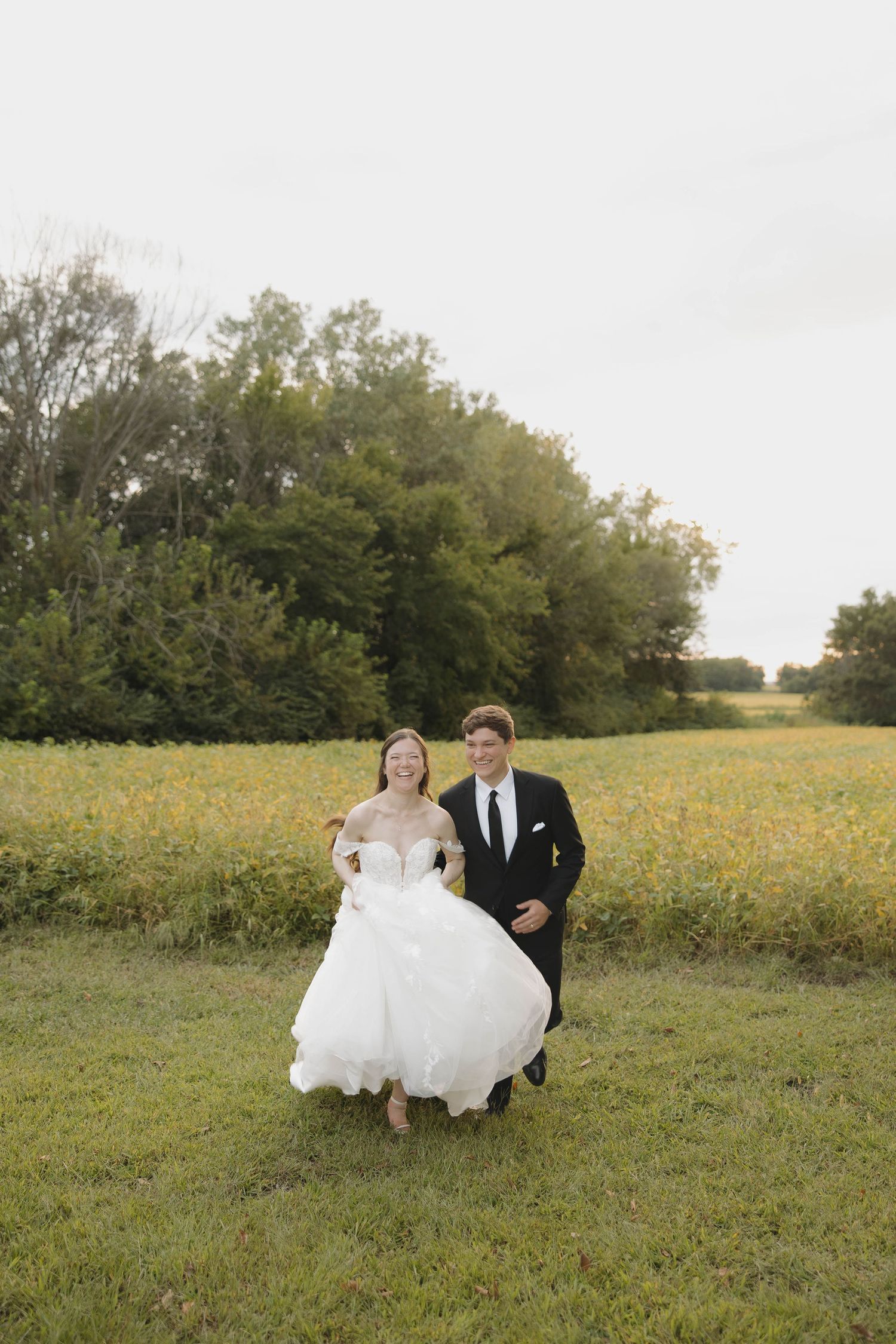 A couple walks together through a golden meadow during an outdoor wedding photoshoot.