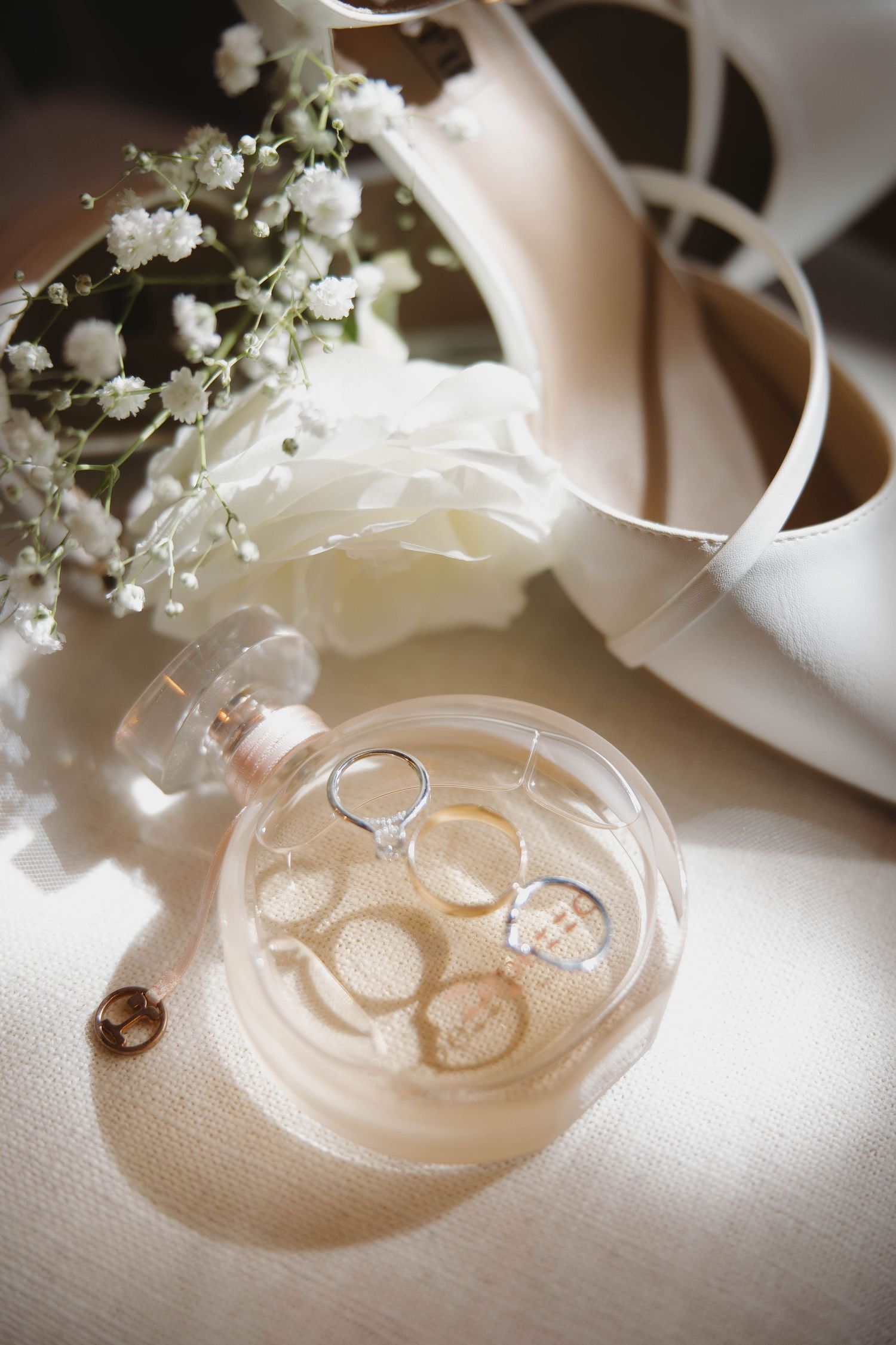 Wedding rings presented elegantly on a glass dish with delicate baby's breath flowers and soft lighting.