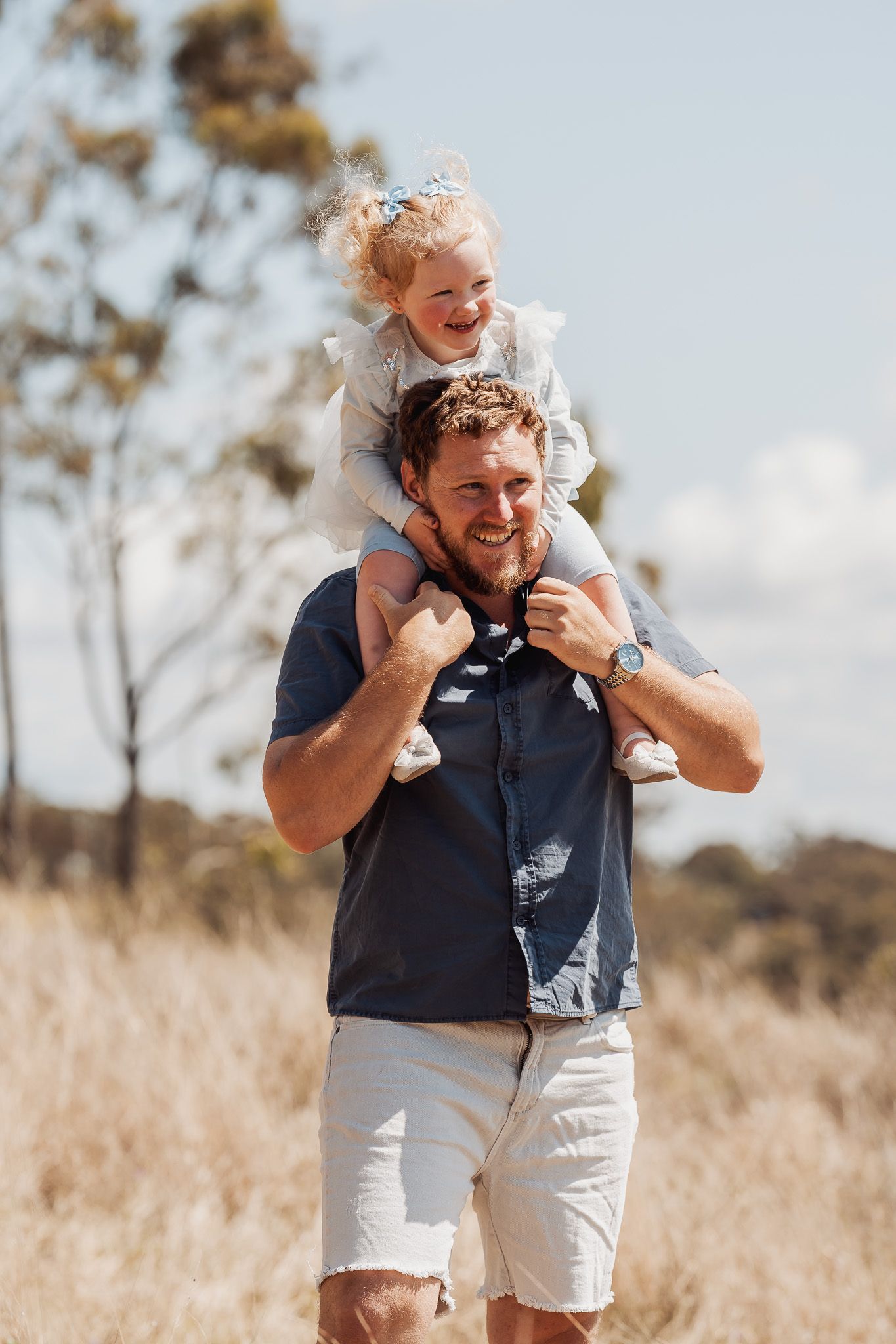 Parent and child playing together in a sunny field with trees in the background.
