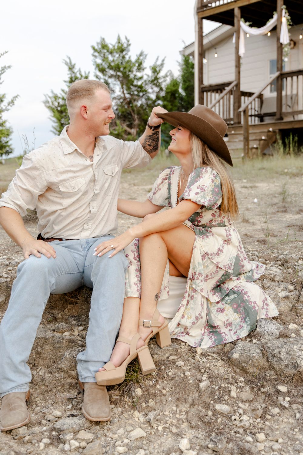 Couple posing in Dripping Springs, Texas Hill Country with a cowboy hat during romantic engagement session.