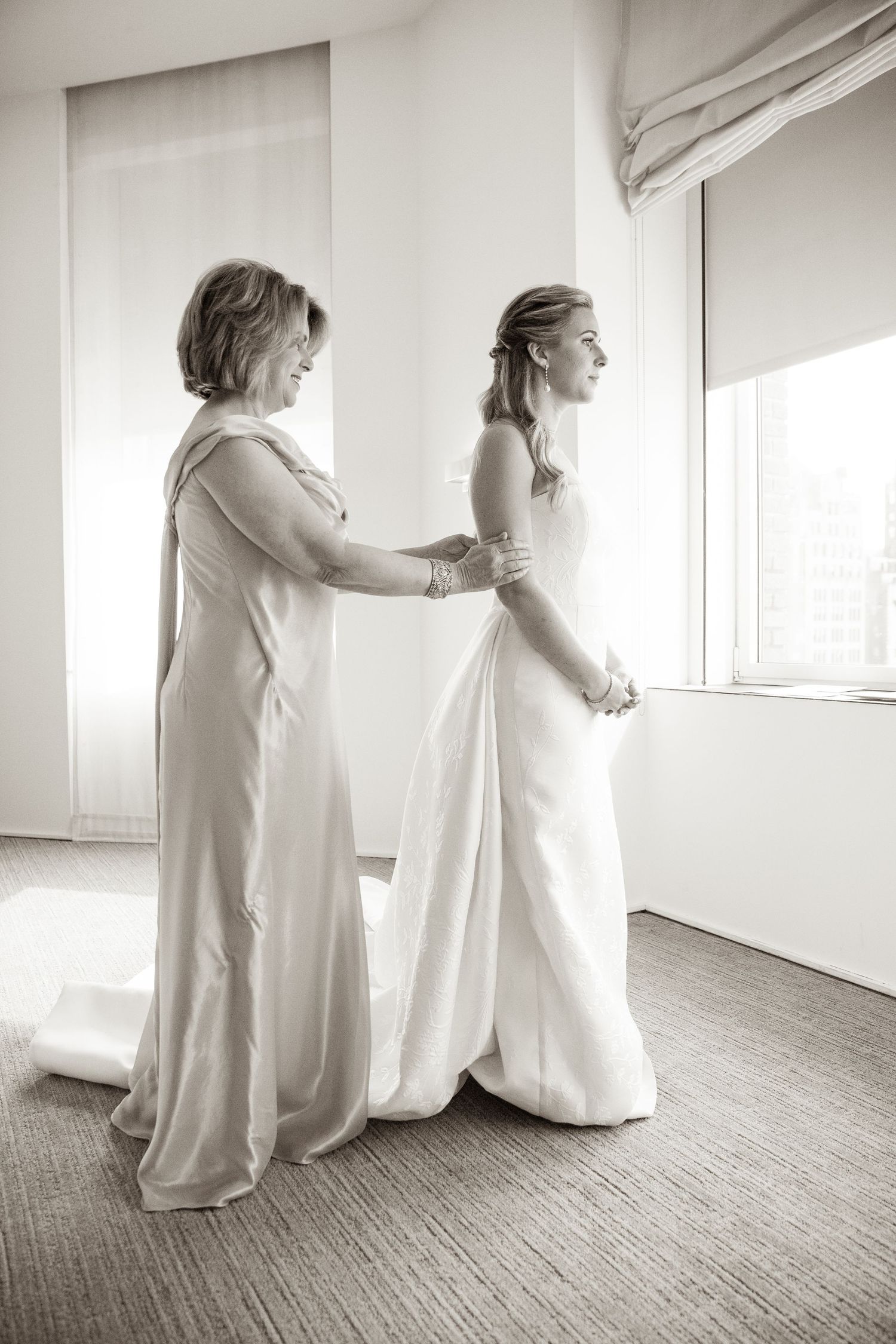 Black and white photo of bride getting help with dress preparations.