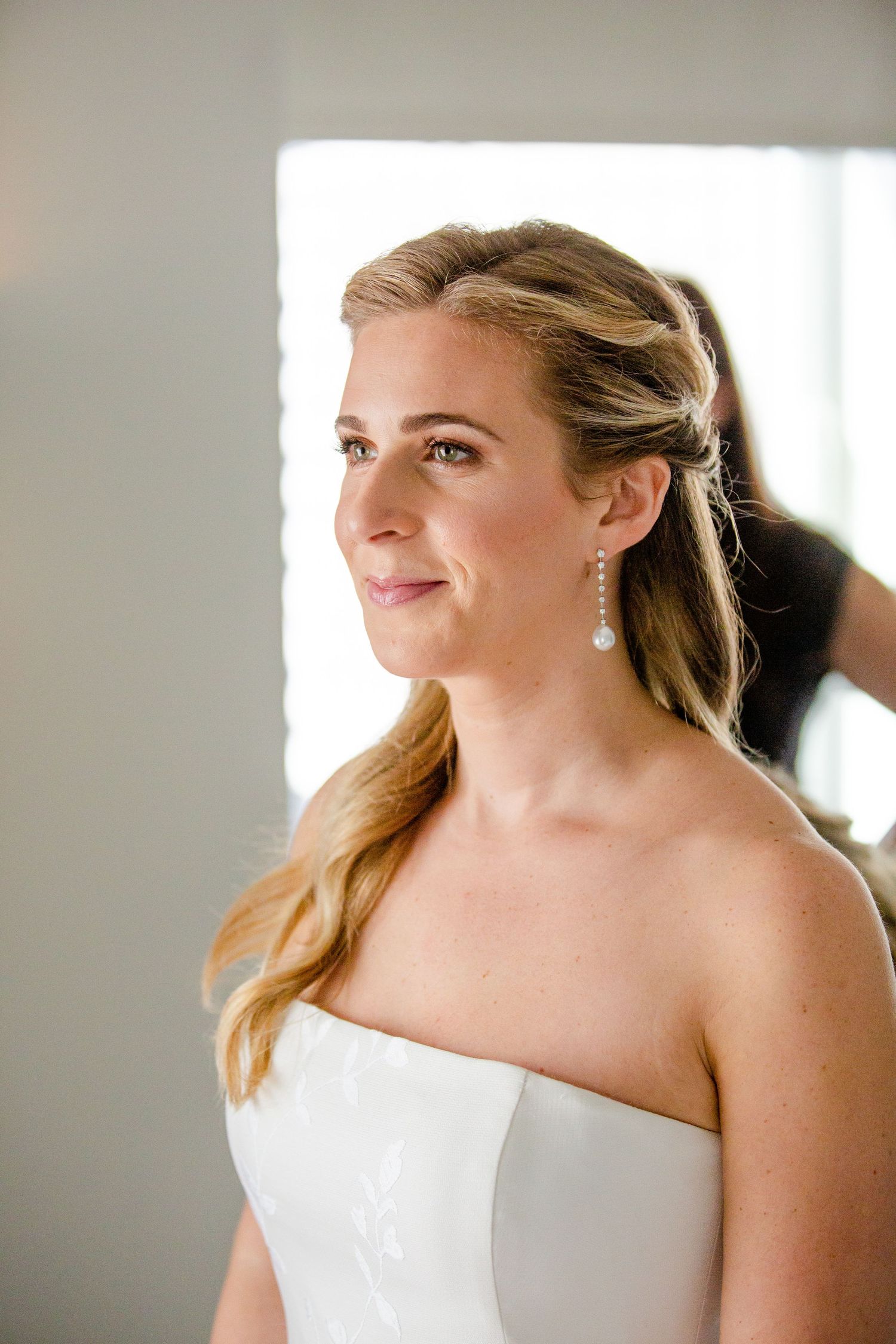 Bride in strapless white gown with elegant hair and earrings.