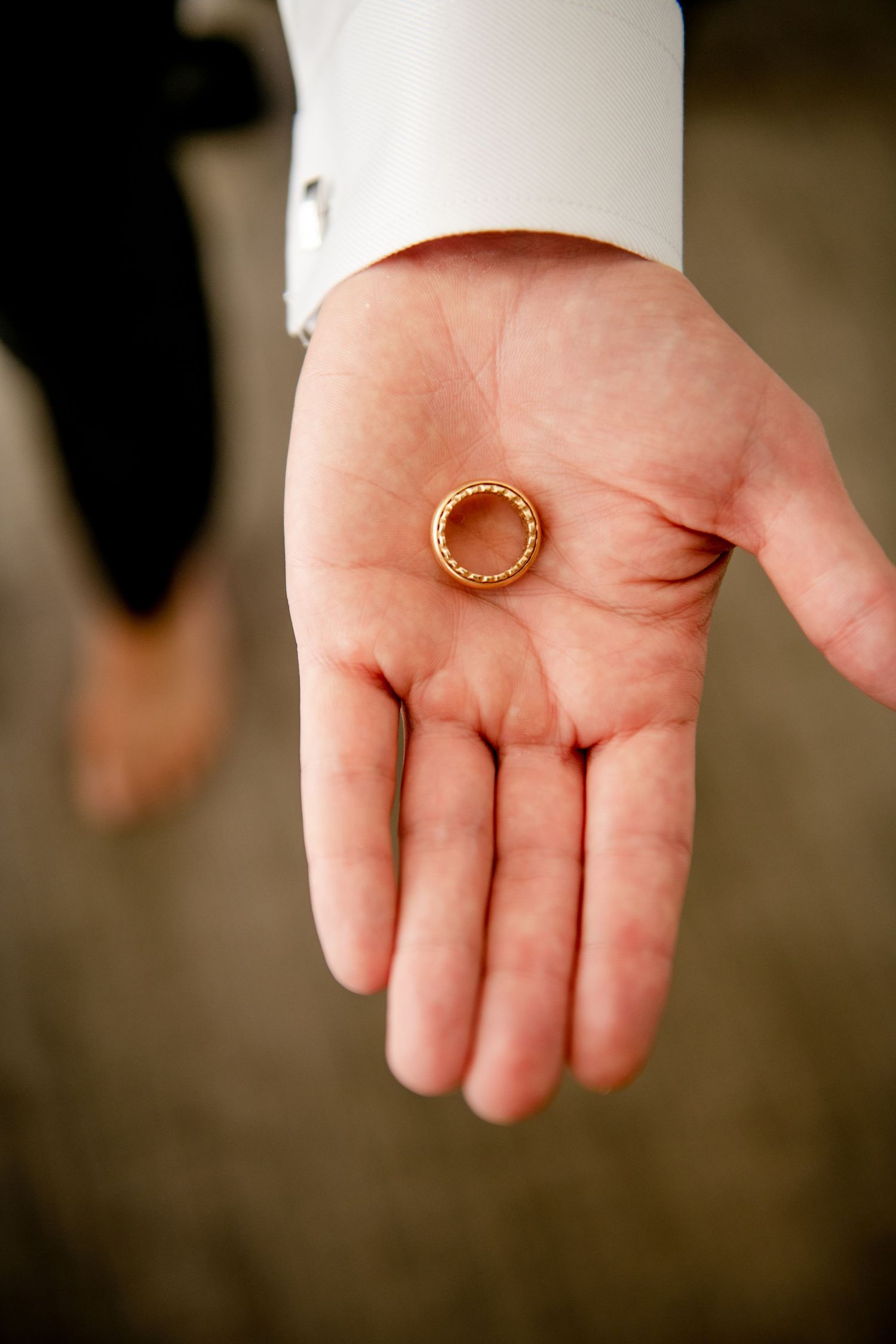Wedding ring held in an open palm with white sleeve visible.