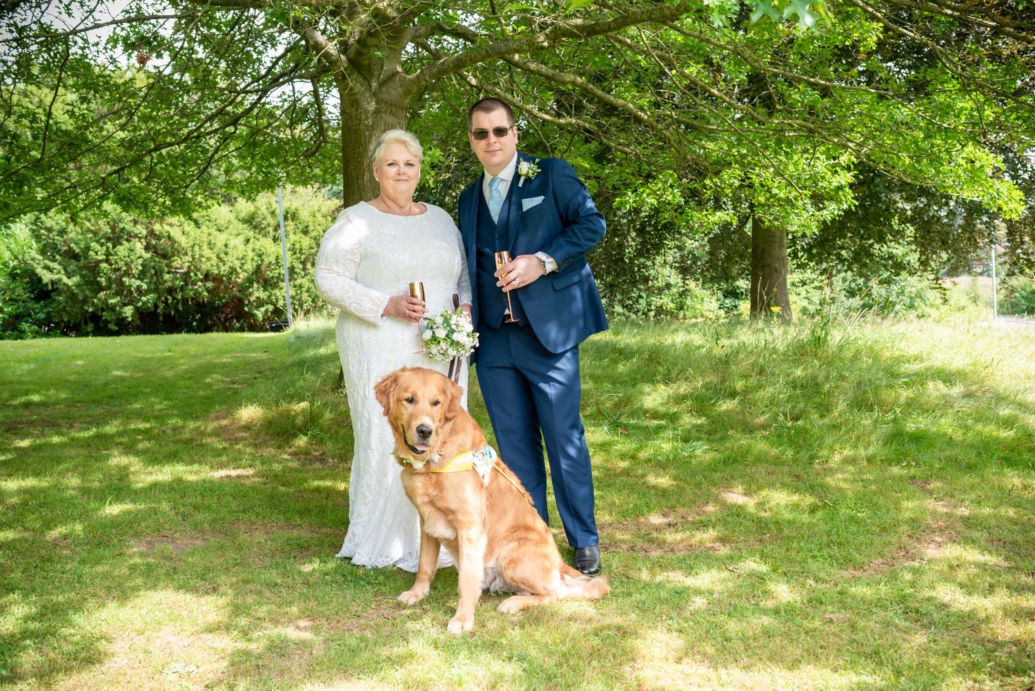 Newly married couple with their service dog at Mold Registry office grounds holding champagne flutes by photographer Michael Pardoe