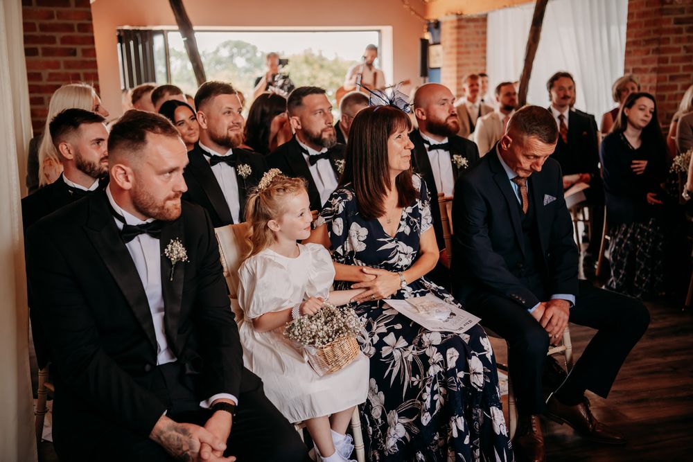 Wedding guests laugh and smile while seated at tables during an elegant indoor reception at a brick-walled venue.