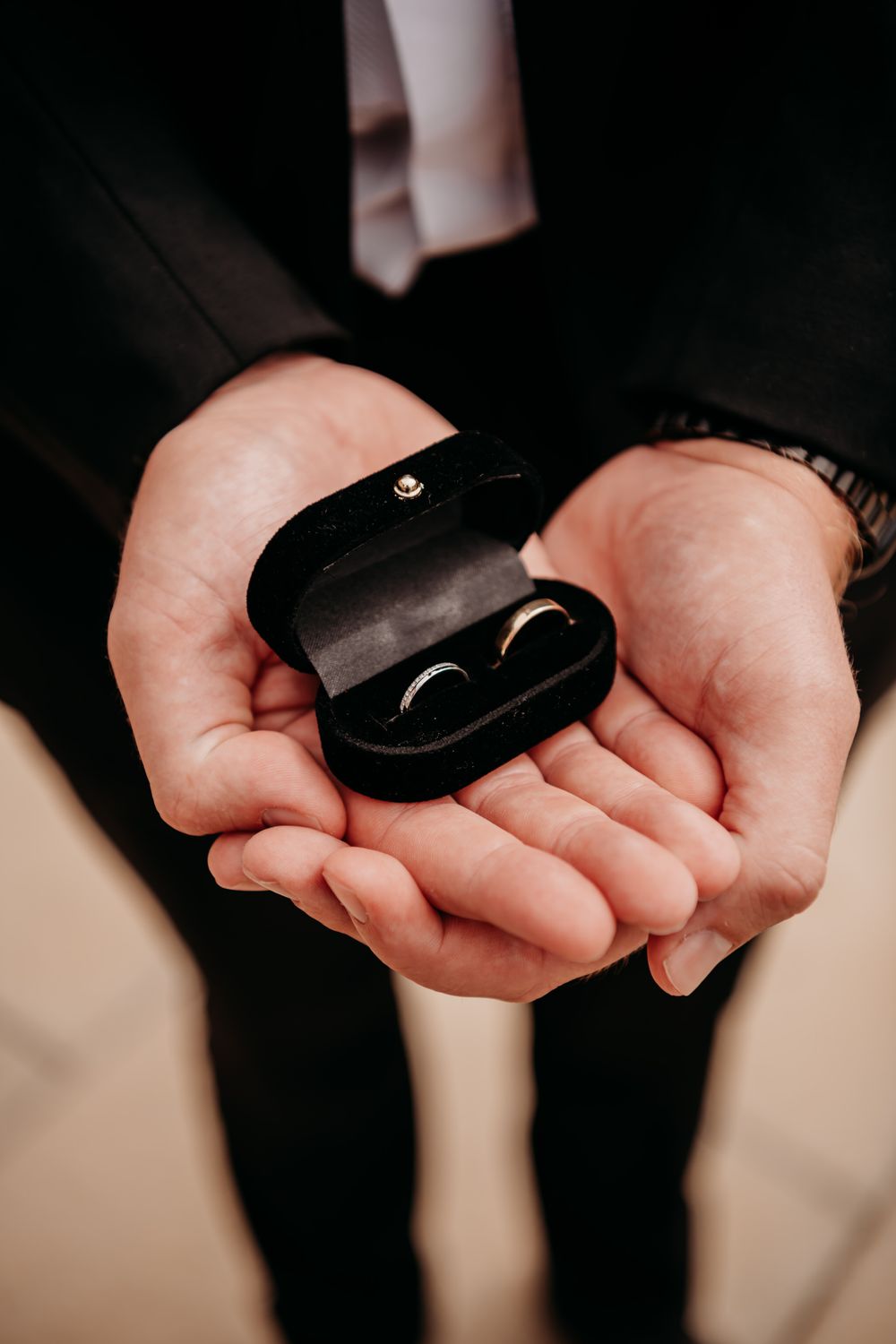 Close up view of hands holding a black ring box with wedding band against dark background.