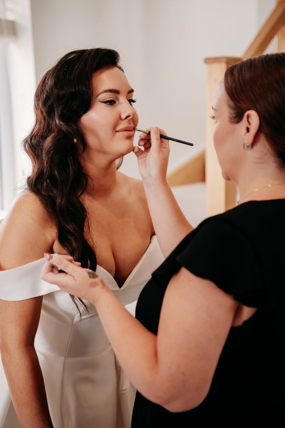 Makeup artist carefully applies cosmetics during a professional beauty session in a bright indoor setting.