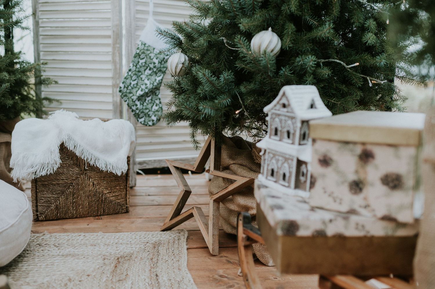 White ceramic Christmas village houses and winter decor arranged with evergreen branches and rustic natural elements.
