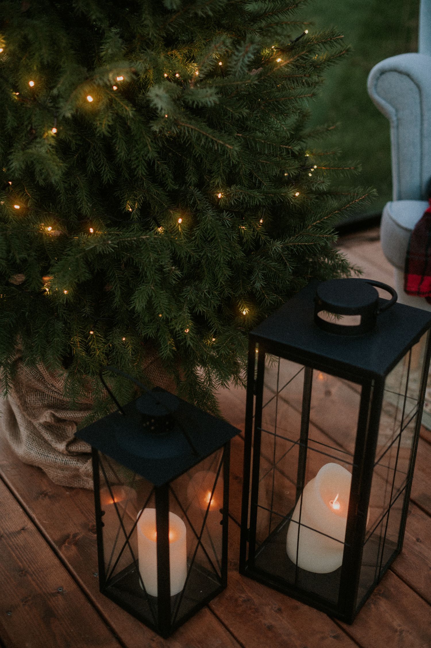 Black metal lanterns with candles arranged under an illuminated Christmas tree on a wooden floor.