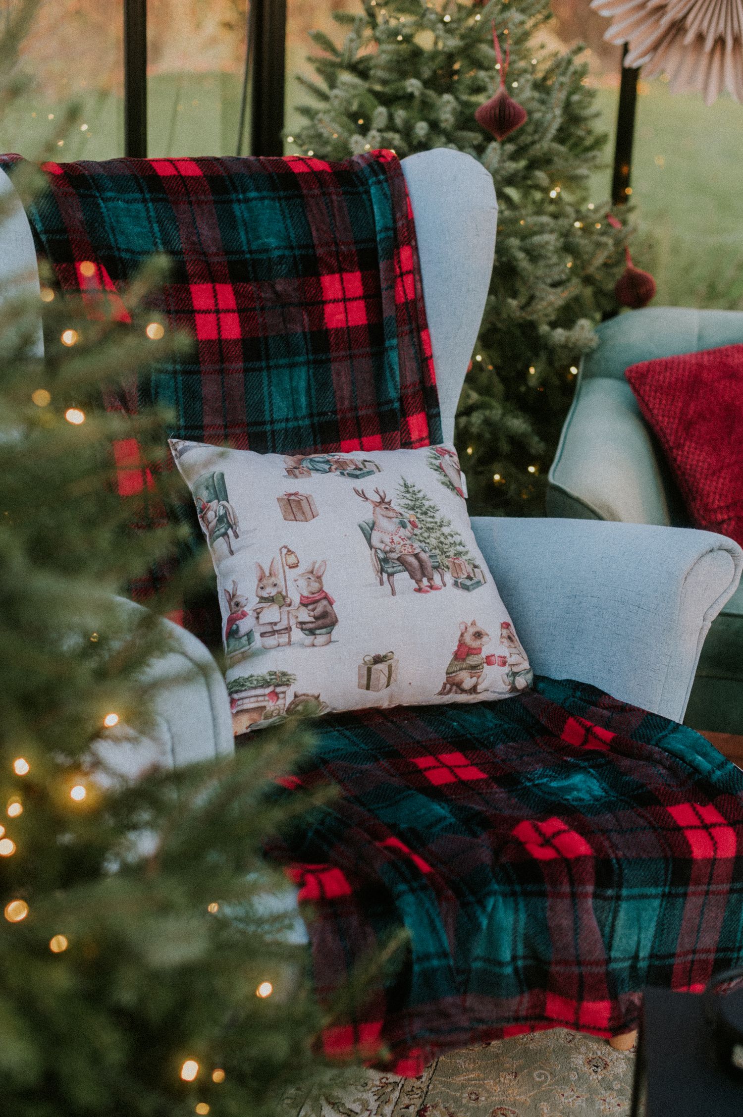 Cozy Christmas decor featuring plaid blankets and decorative throw pillows with holiday designs arranged on a chair.