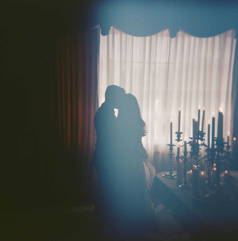 A romantic silhouette of a couple in a candlelit room with white curtains and candlesticks creating a moody atmosphere.