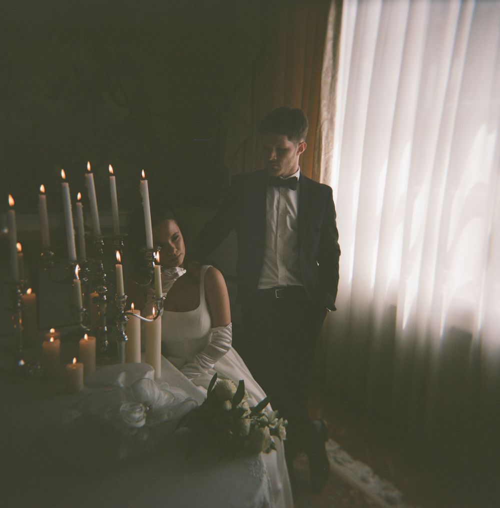 A couple in wedding attire poses in a moody room with lit candelabras creating a romantic ambiance.