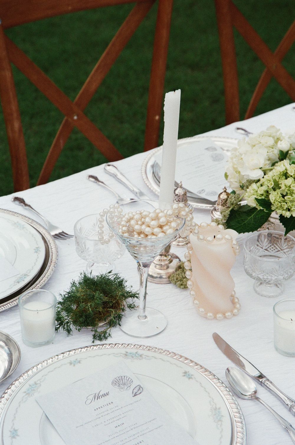 Elegant wedding table setting with white linens, crystal glasses, pearls, and hydrangea floral arrangements on a formal dining table.