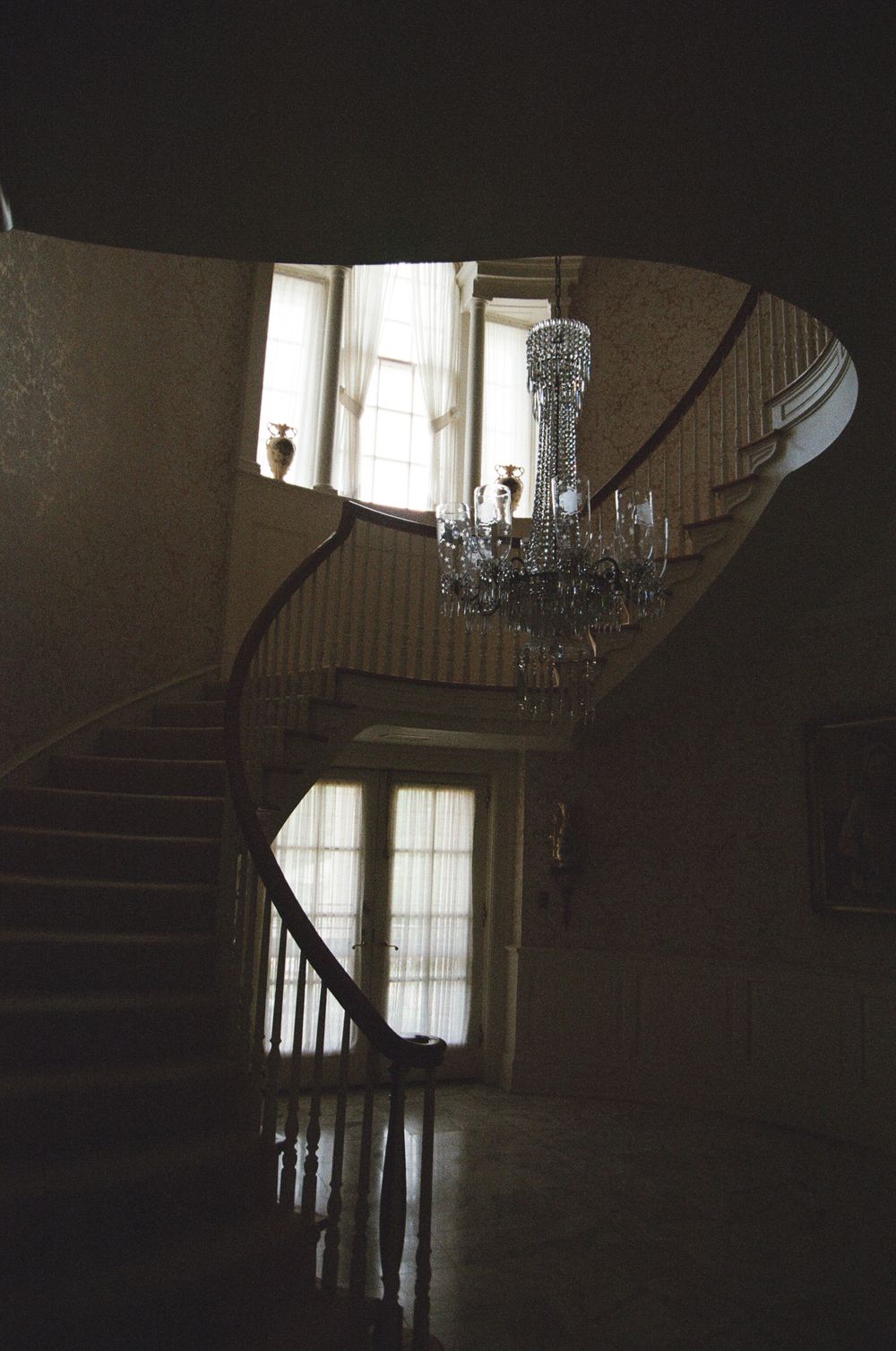 A dark moody interior staircase with a crystal chandelier hanging in an elegant curved stairwell with natural light.