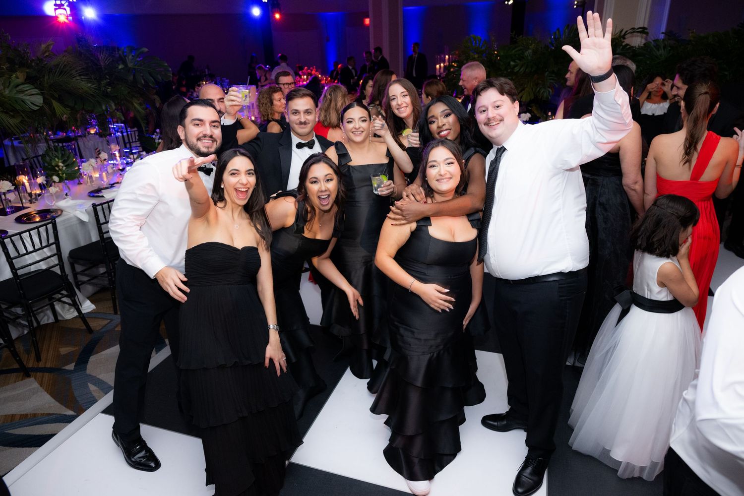 Lively wedding reception dance floor filled with guests celebrating and dancing under purple spotlights.