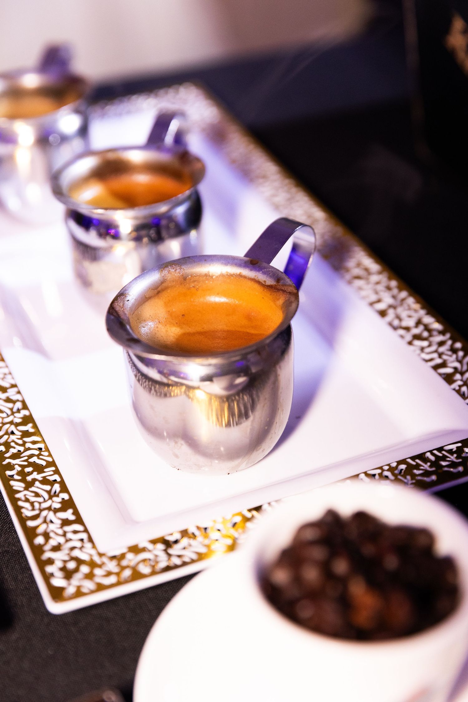 Hot espresso served in elegant silver cups with decorative white napkins and chocolate truffles on a dark surface.
