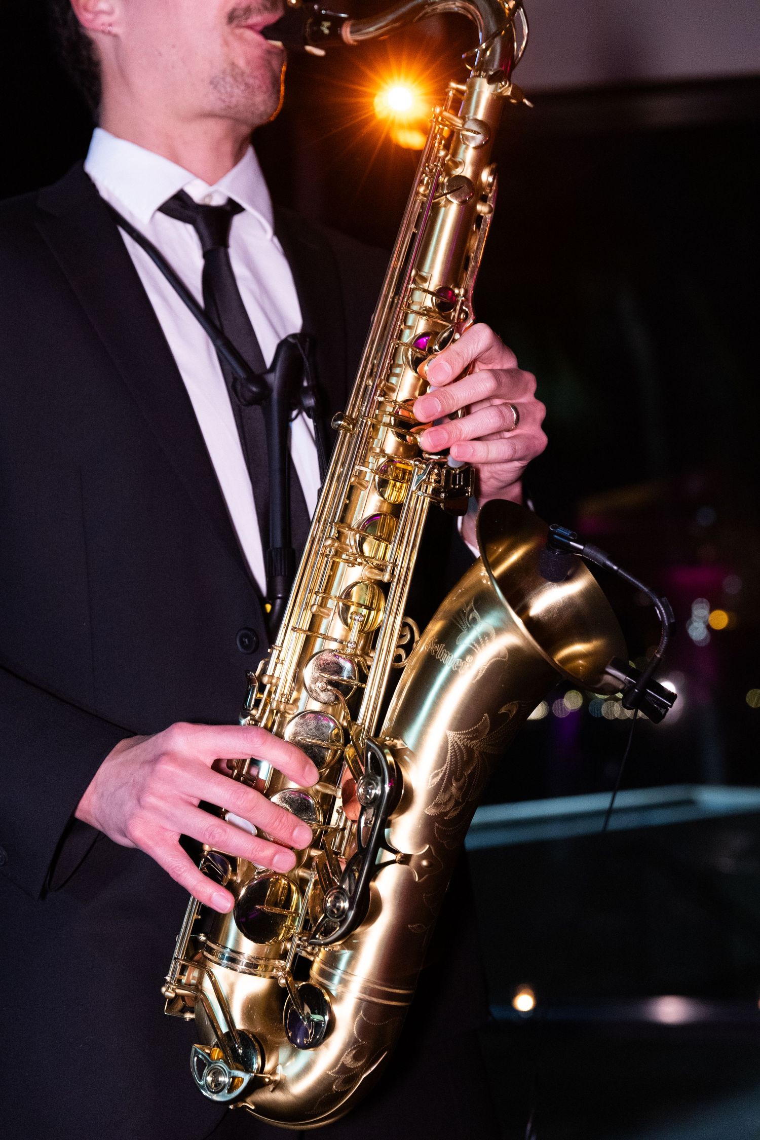 Professional jazz saxophone musician in formal attire performing on stage with dramatic lighting and dark background.