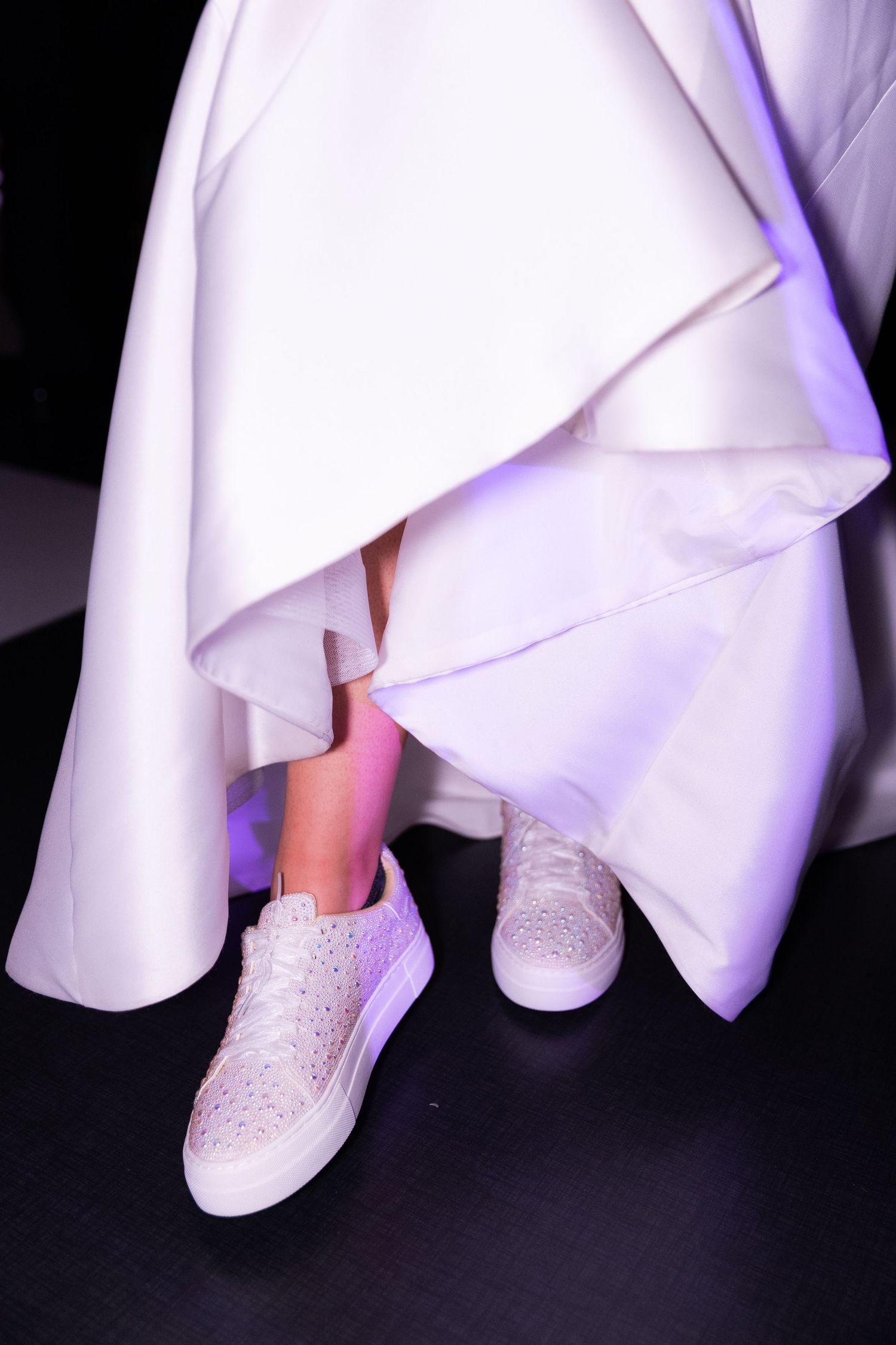 Close-up sequence of white dress hem revealing sparkling rhinestone-covered sneakers underneath.