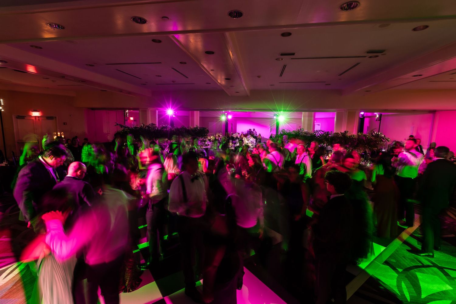Colorful dance floor lights illuminate wedding reception venue with pink and green hues.